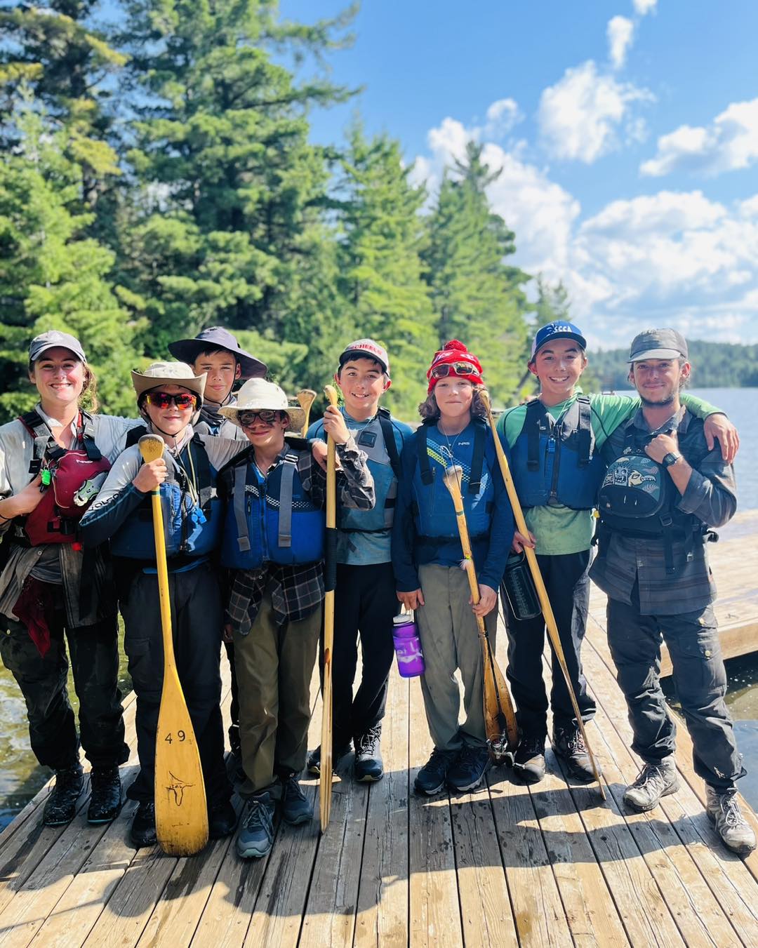 Group of campers with paddles by a lake.