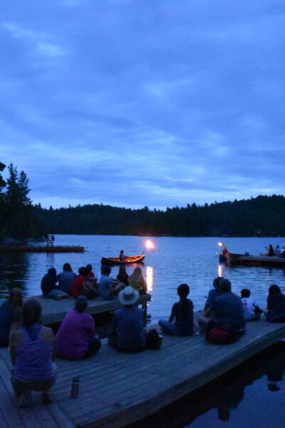 People enjoying a lakeside evening event with canoes.