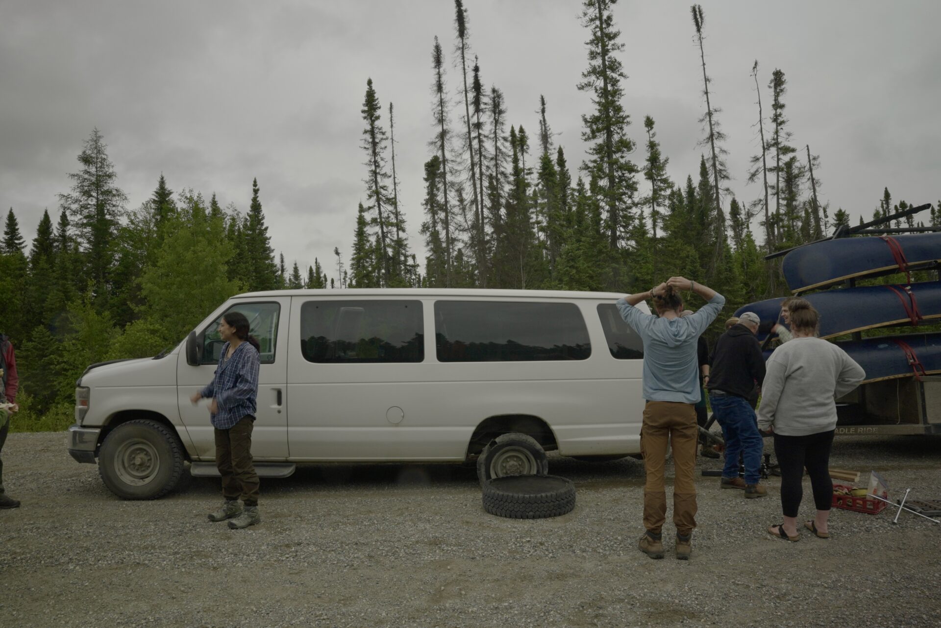 Group changing flat tire by forest.