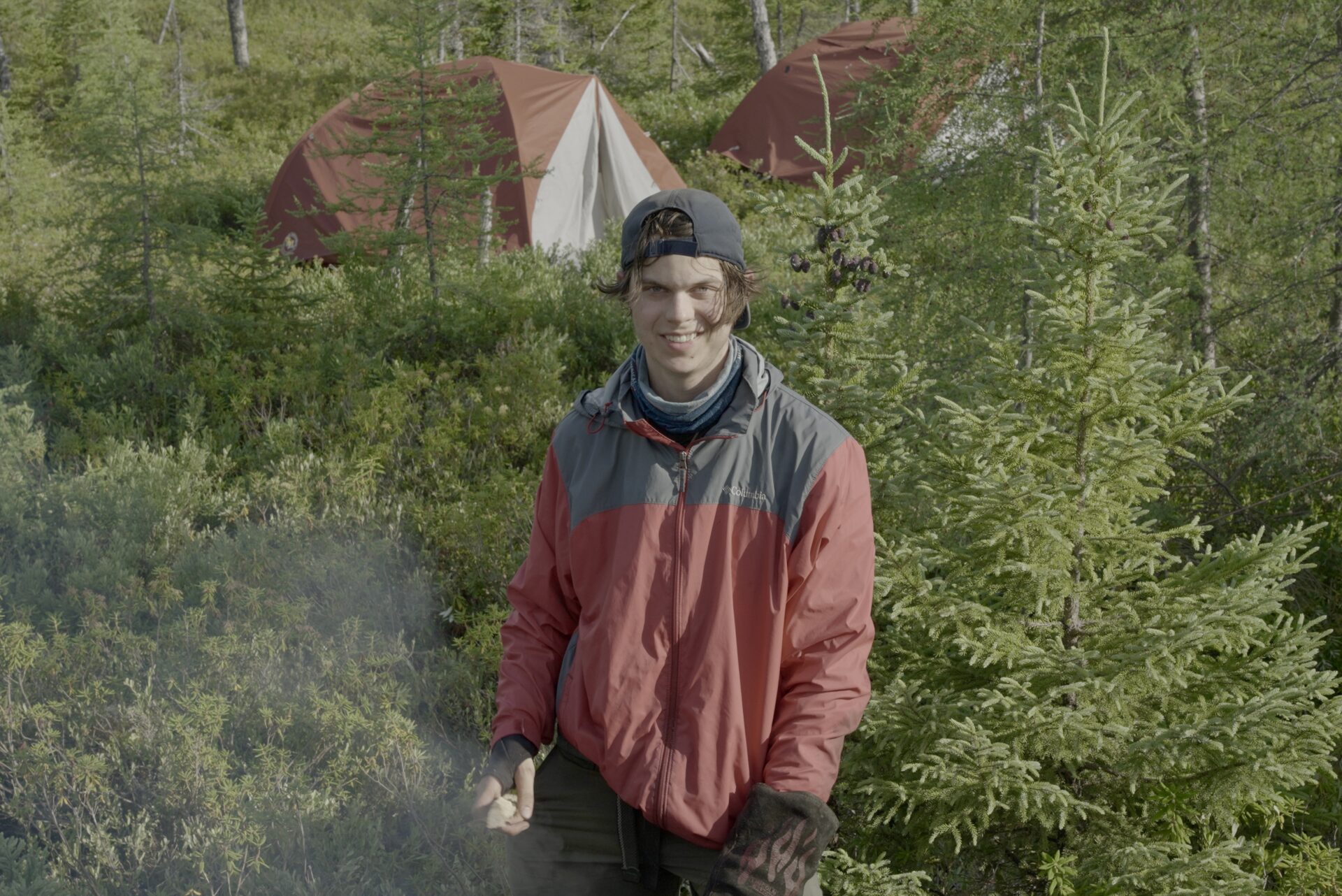 Person camping in the forest near tents.