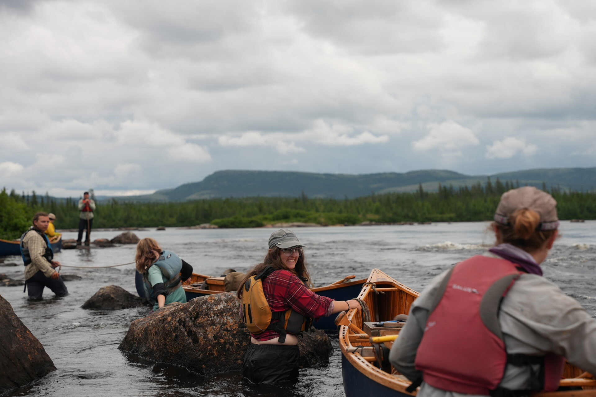 People canoeing in a river with mountains.