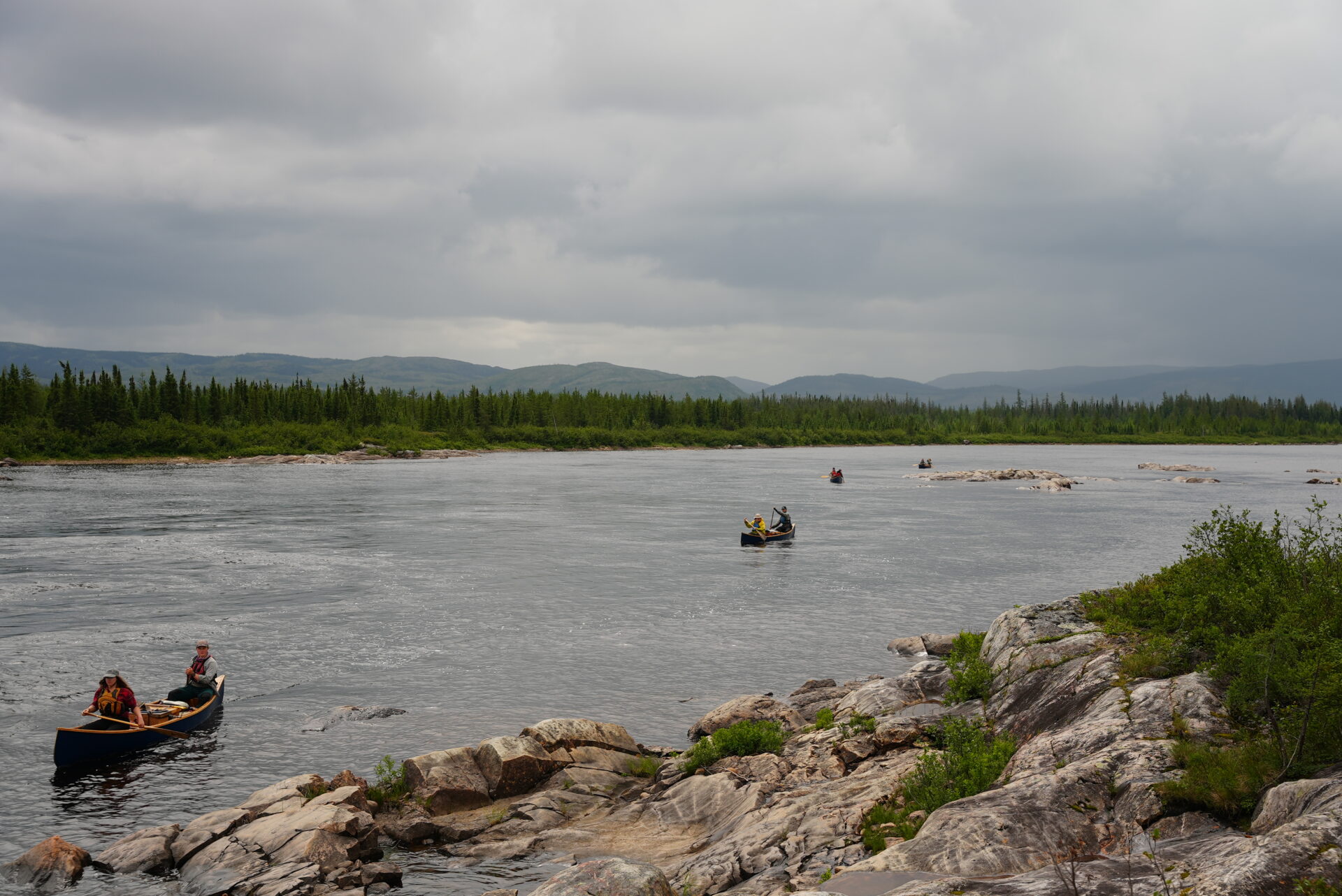 People canoeing on a river with cloudy sky.