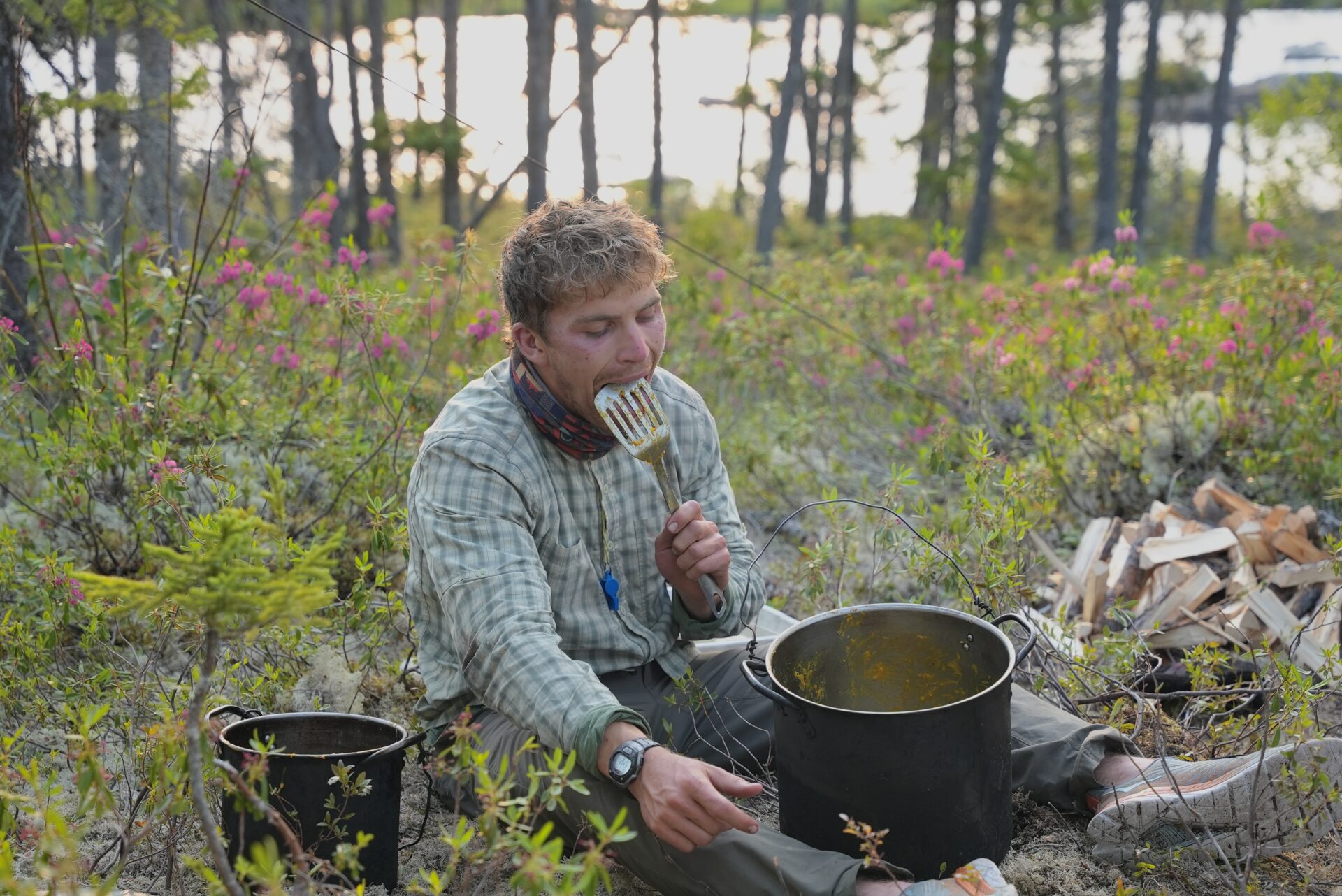 Man camping, cleaning spatula and pot outdoors.