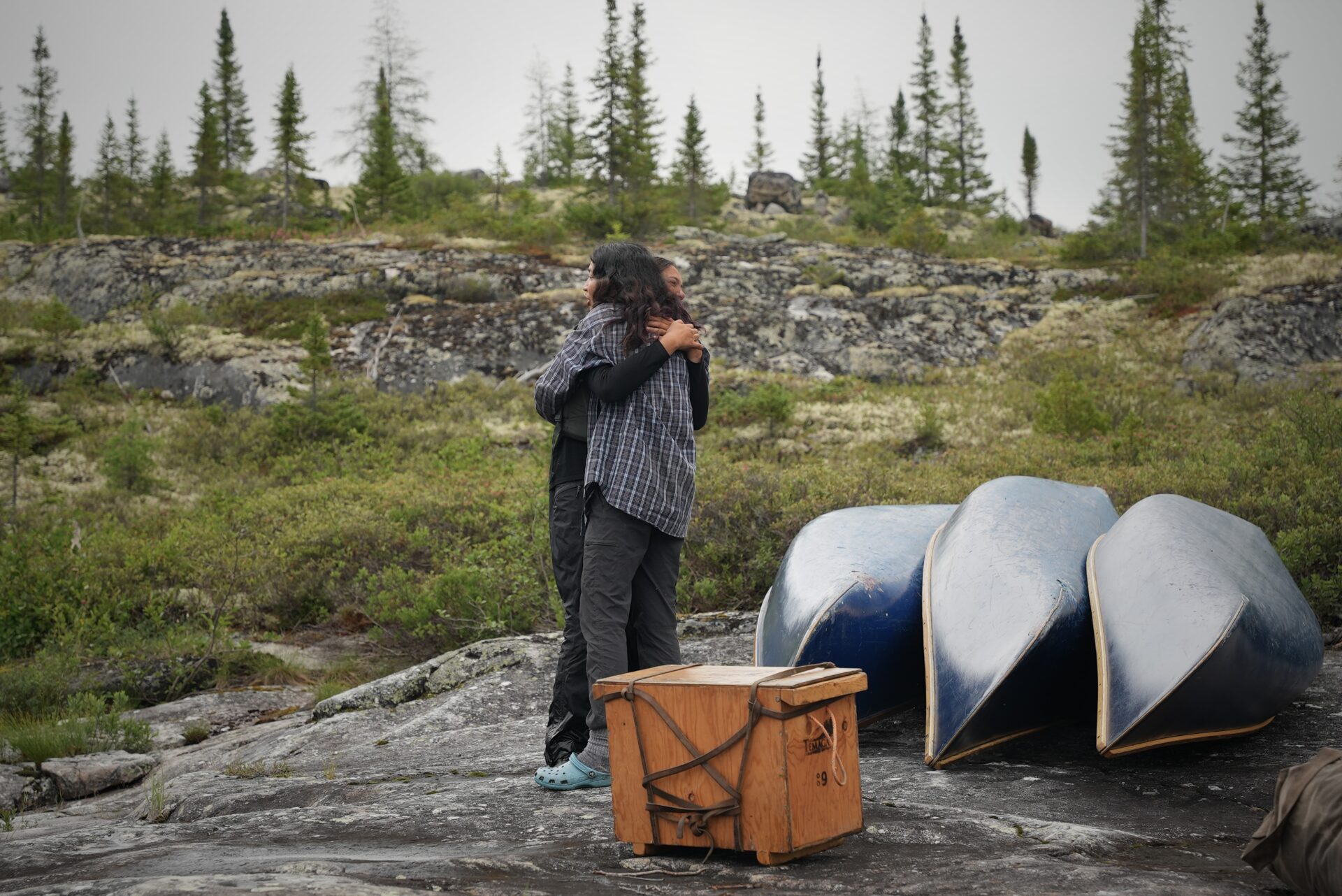 Two people hugging near canoes and a wooden box.