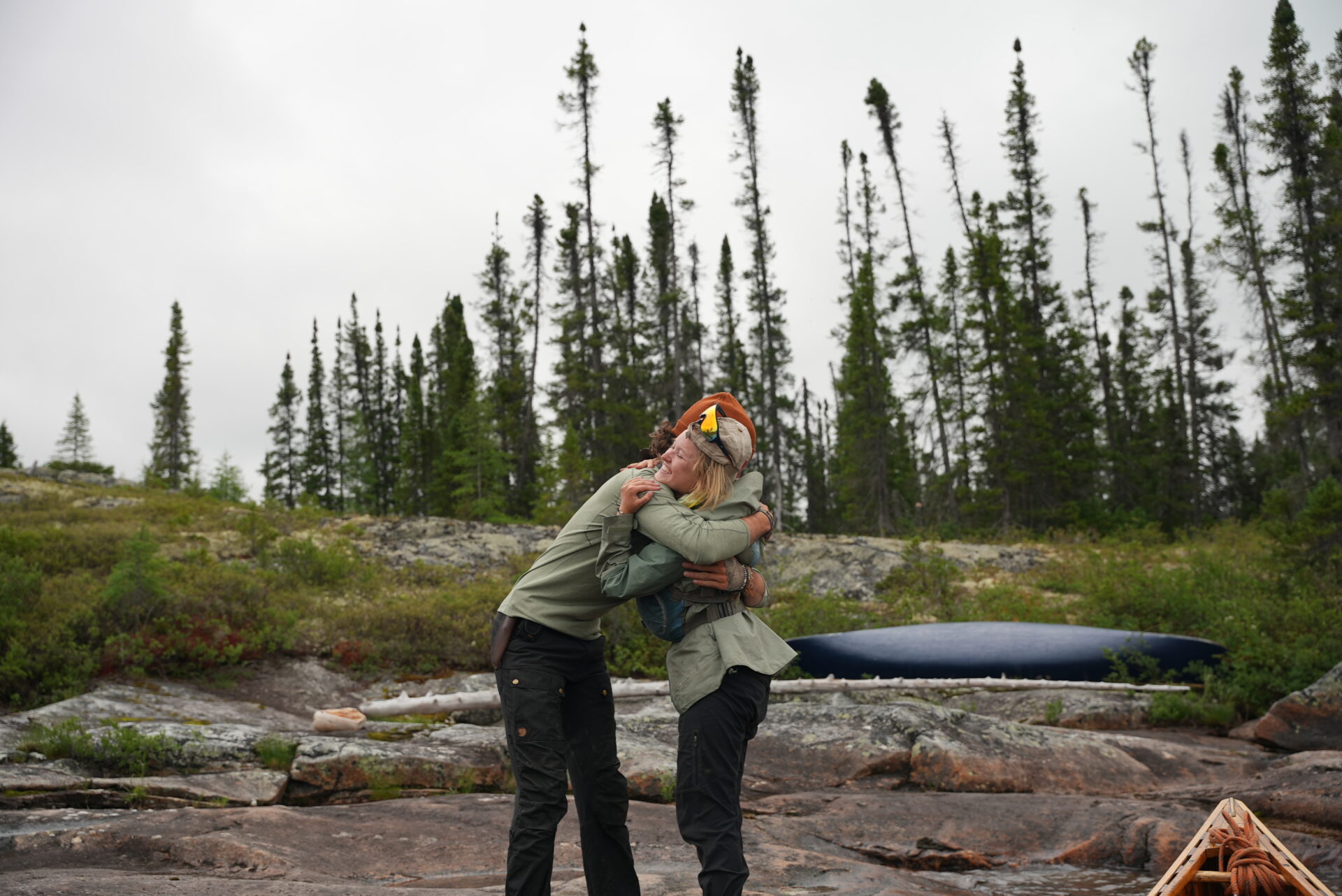 Two people hugging outdoors near canoe.