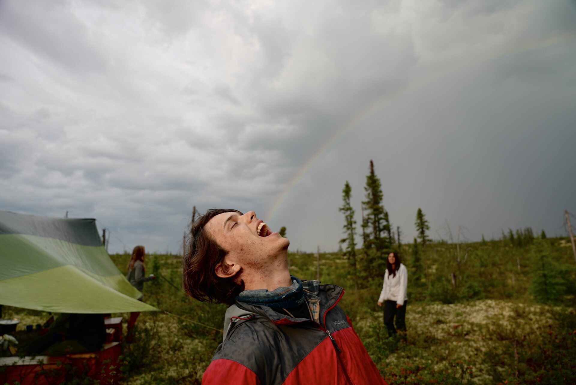 Person laughing outdoors after rain with rainbow.