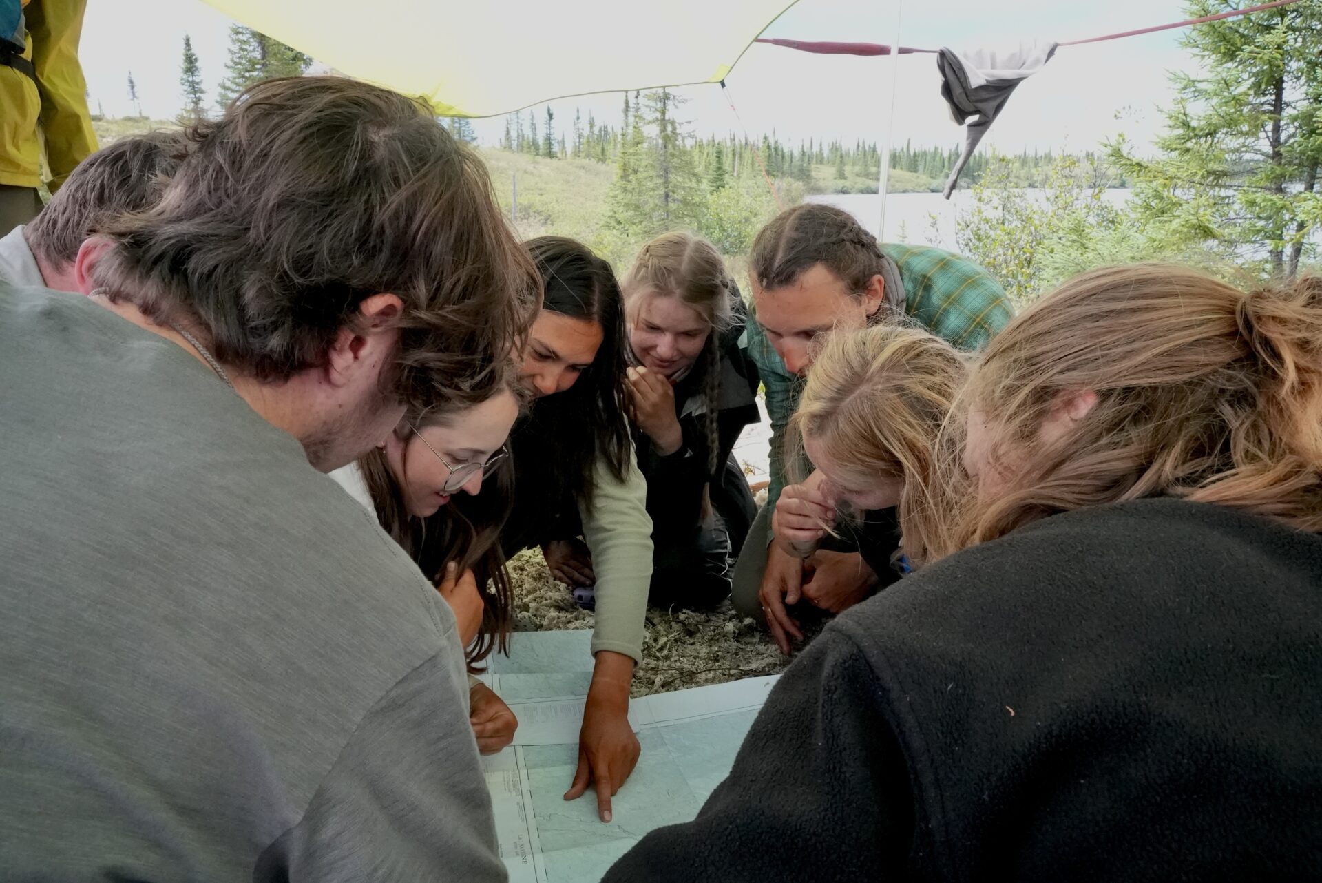 Group studying map outdoors under tent.