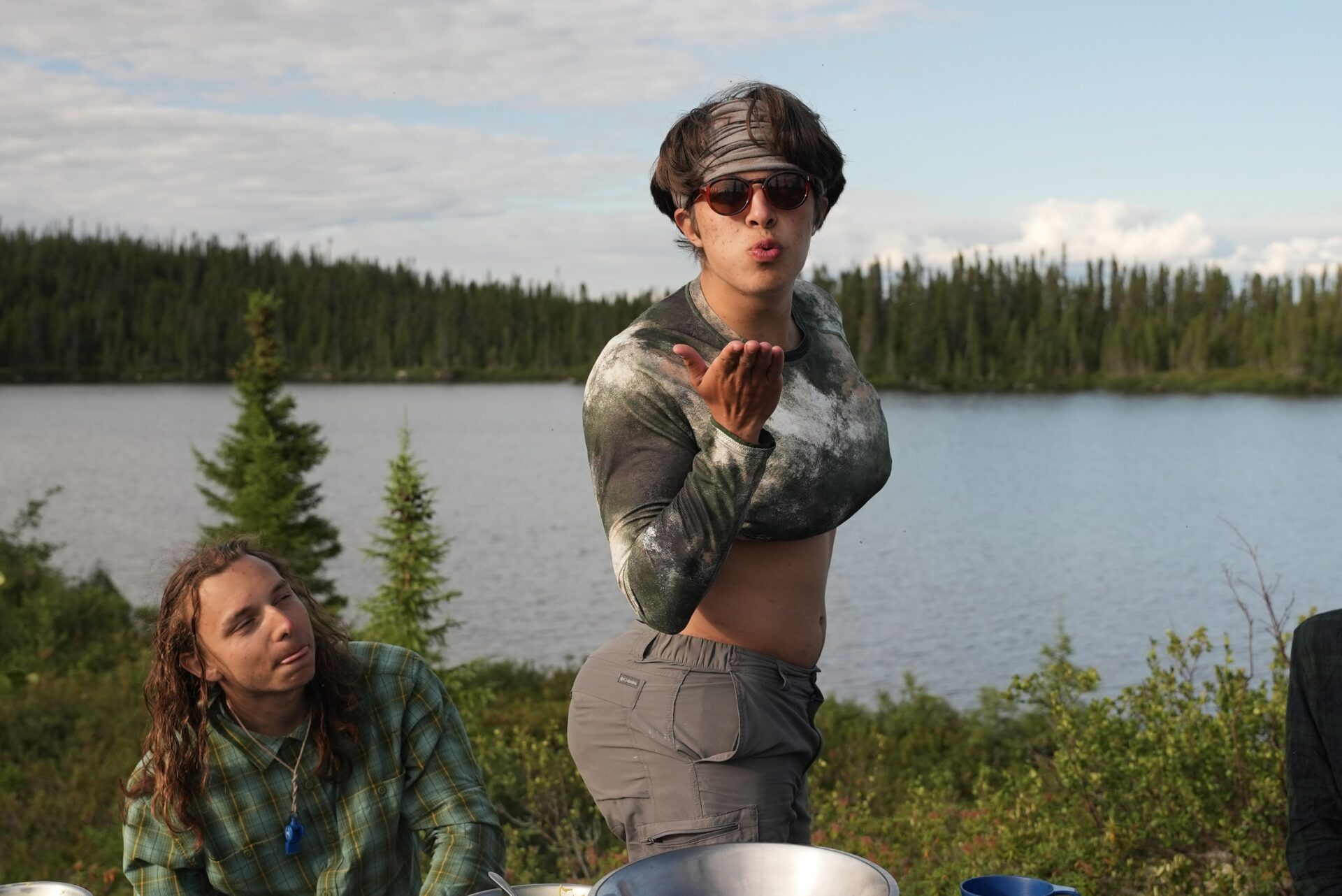 Person blowing kiss by a lake in nature.