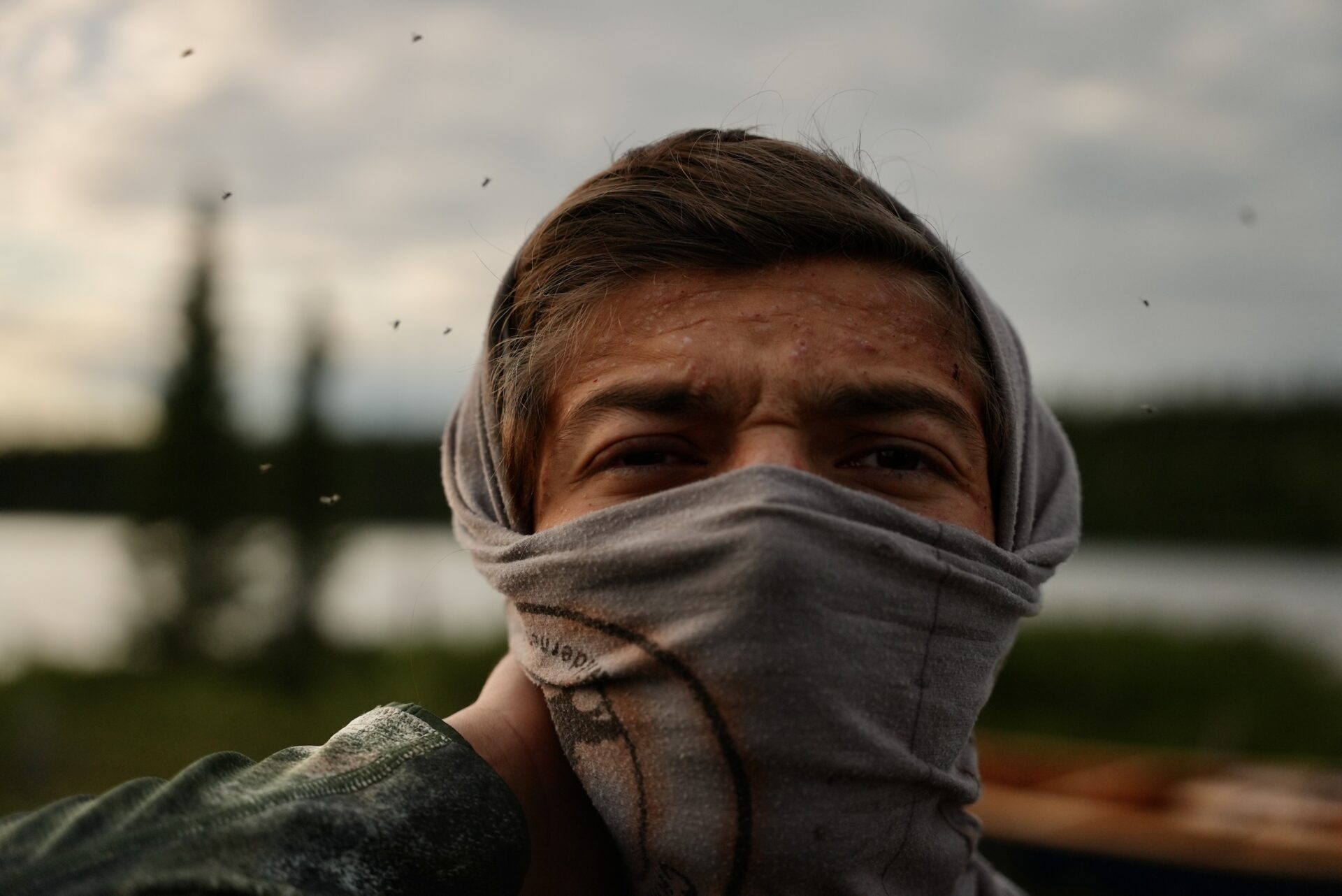 Person outdoors with covered face, mosquitoes flying around.