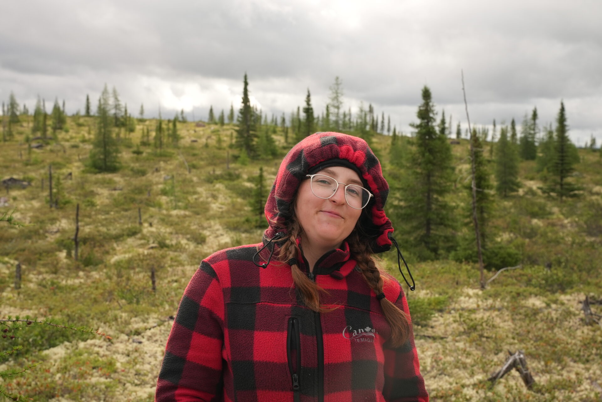 Person in plaid jacket in forested area.