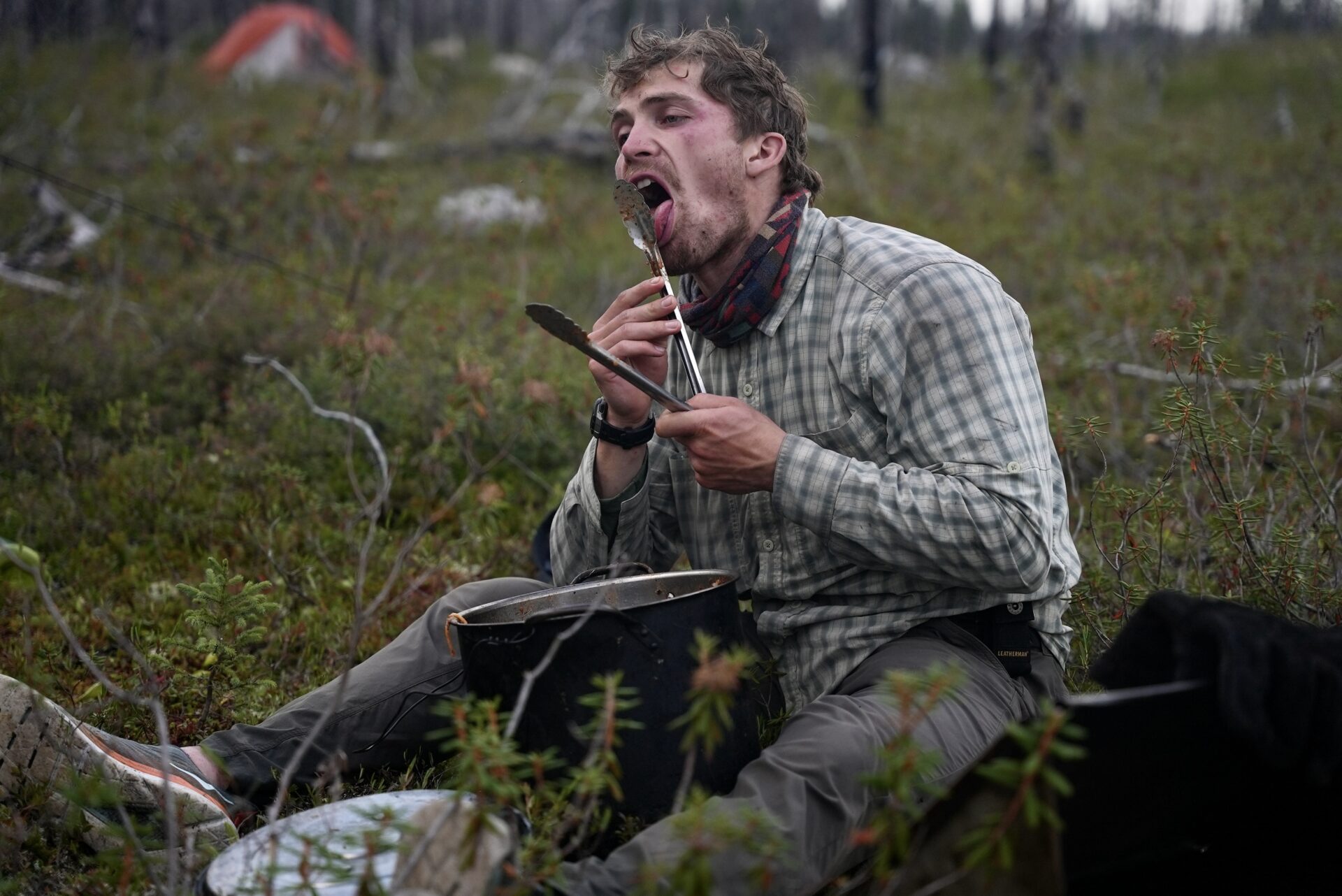 Man camping and eating with cooking tongs