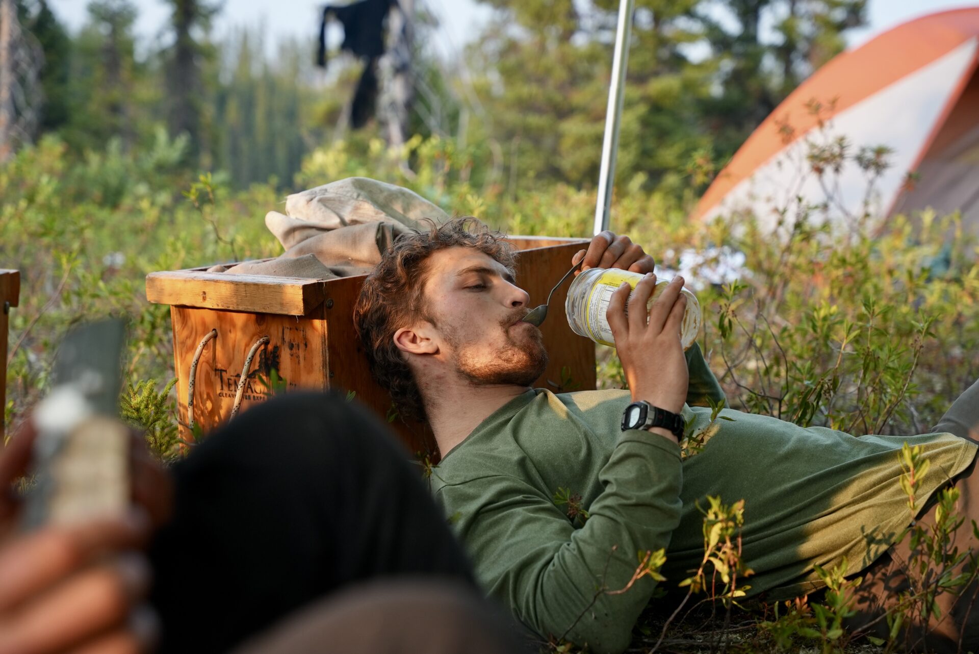 Man eating while relaxing at a campsite.