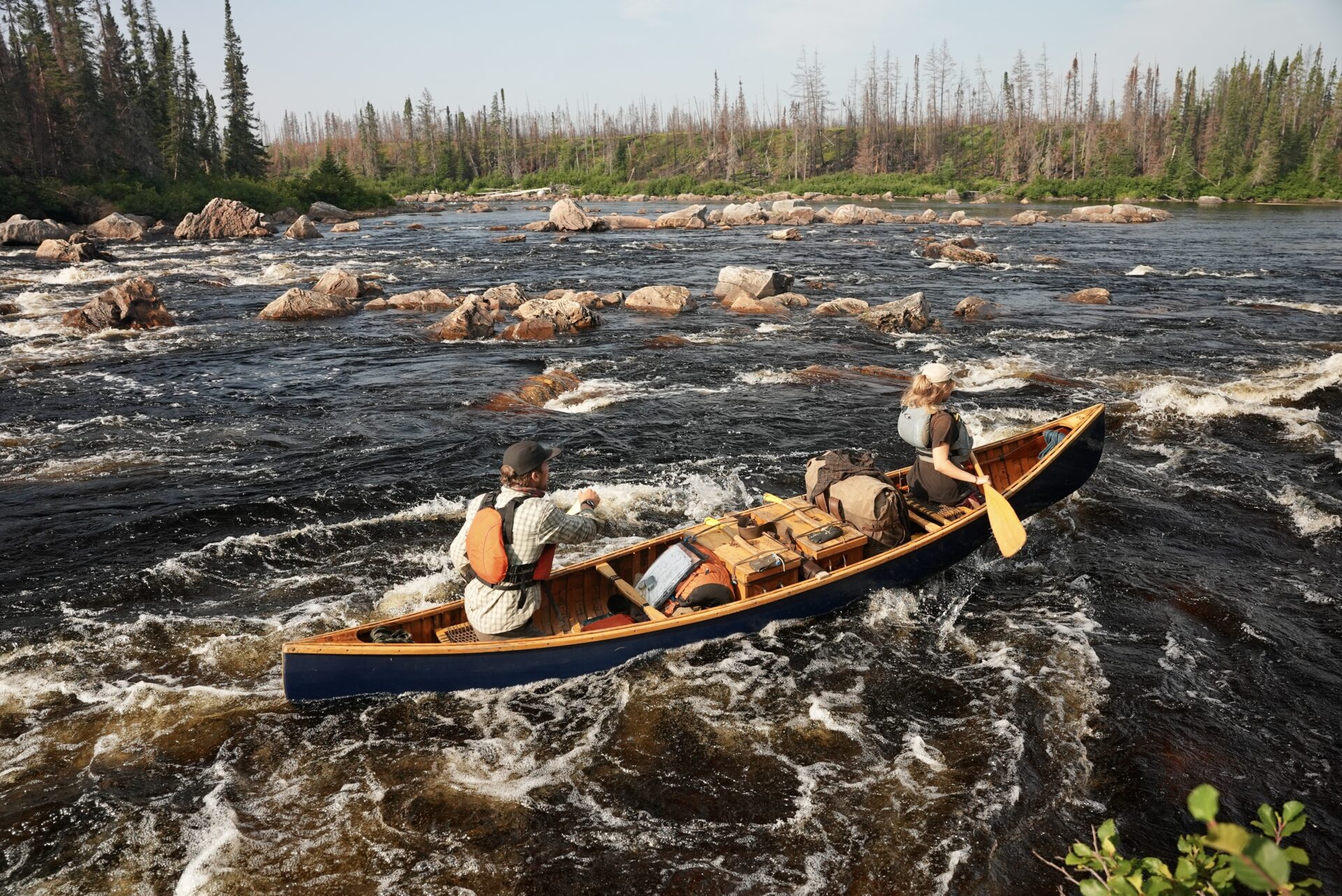 Two people canoeing in a river with rapids.