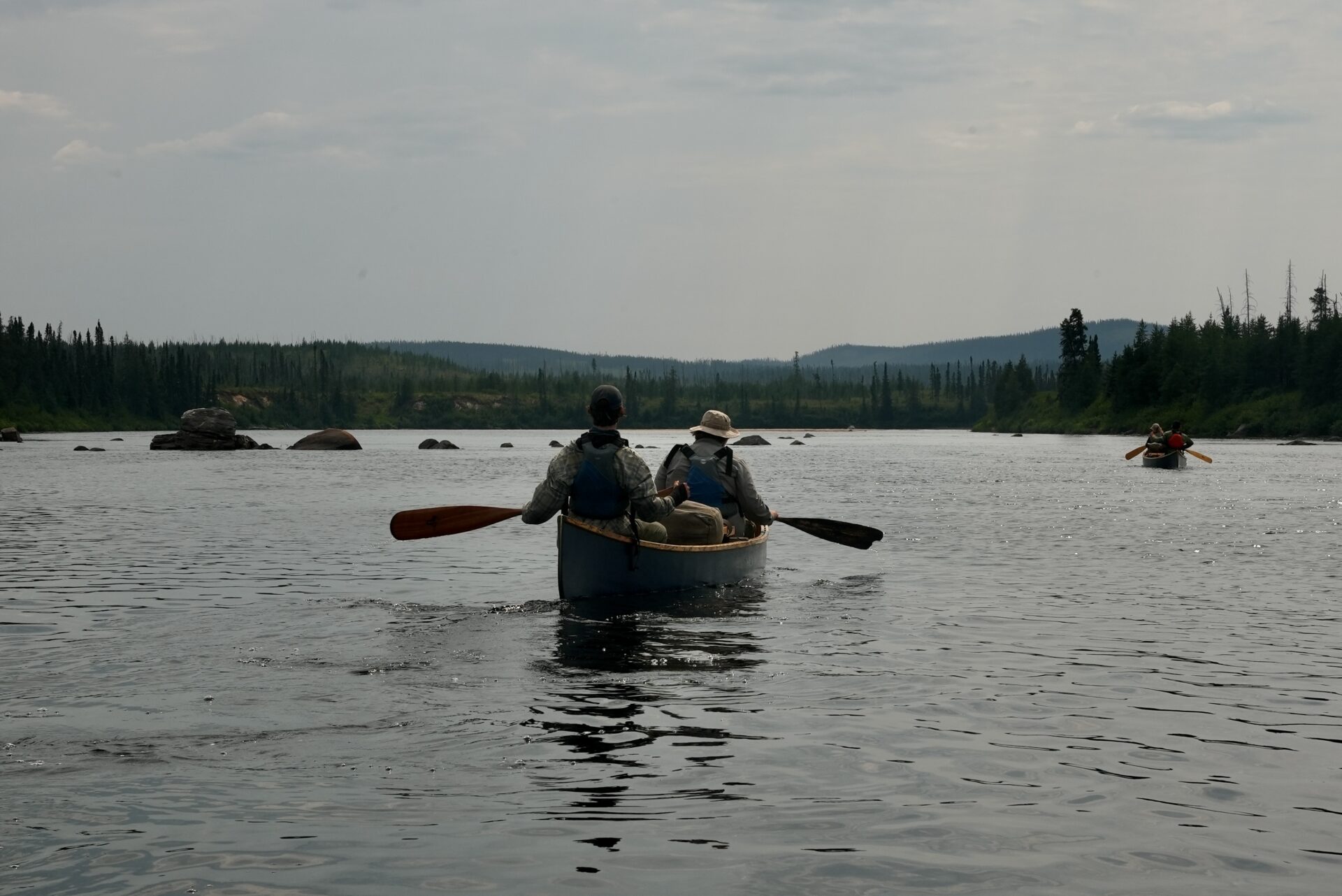 People canoeing on a river in the wilderness.