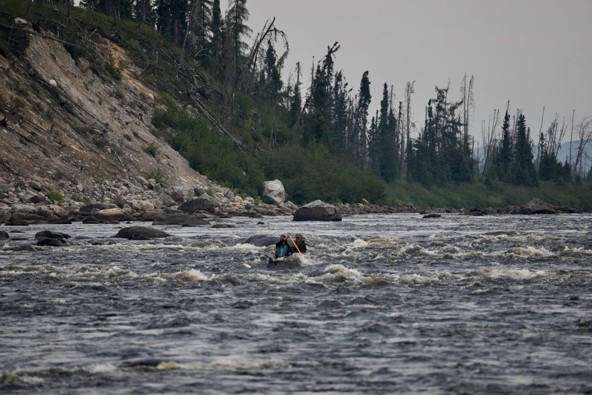 Two people canoeing in rocky, rapid river.