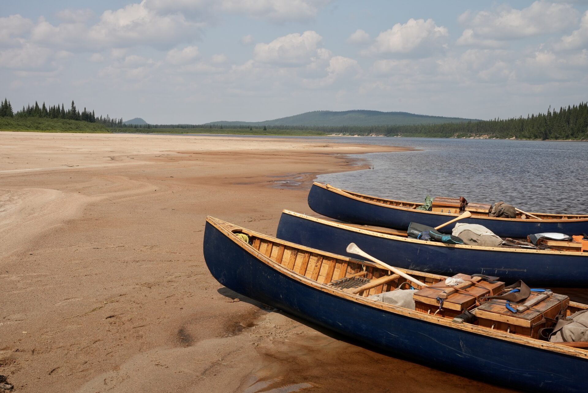 Canoes on sandy shore beside river.