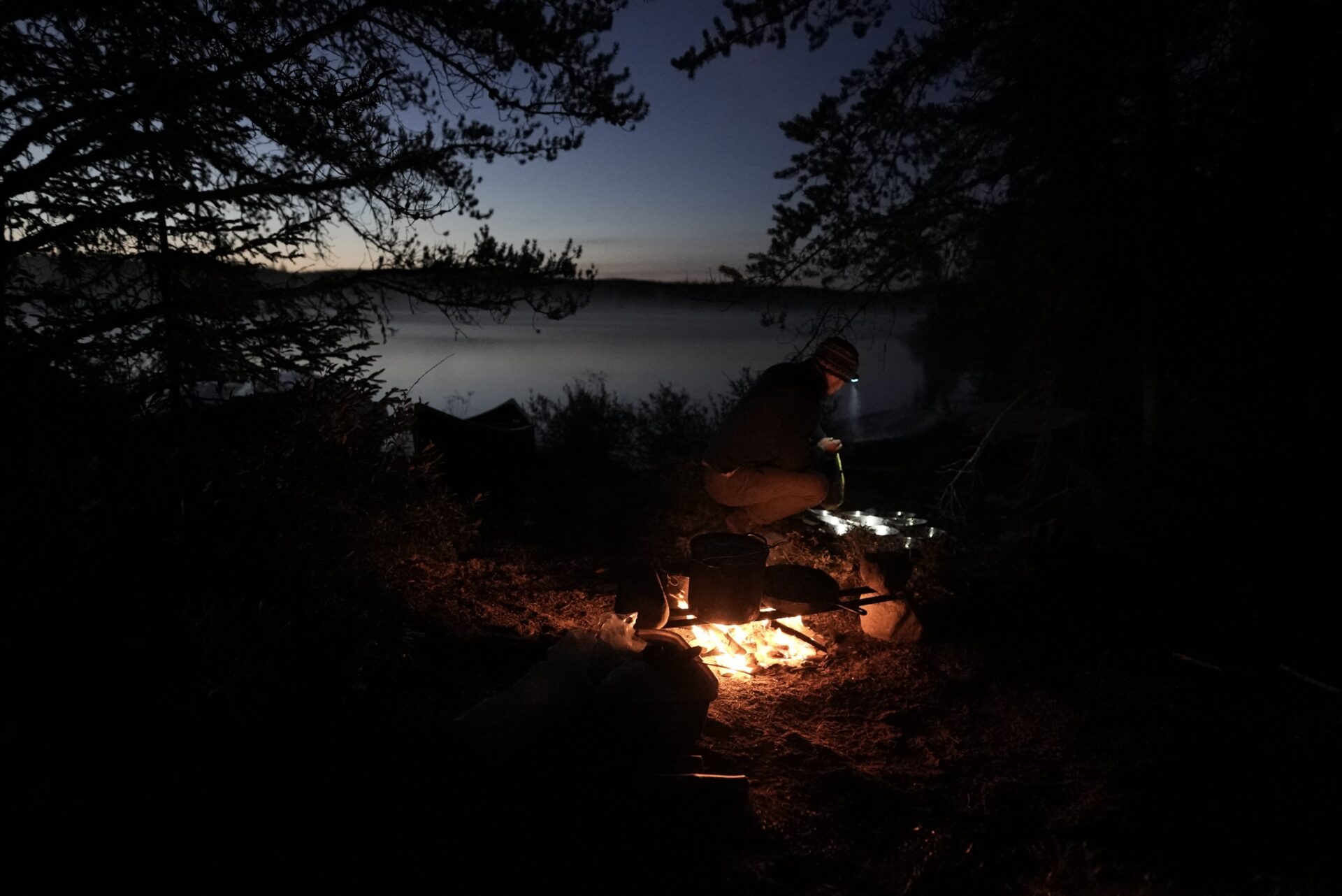 Person cooking at campfire near a lake at dusk