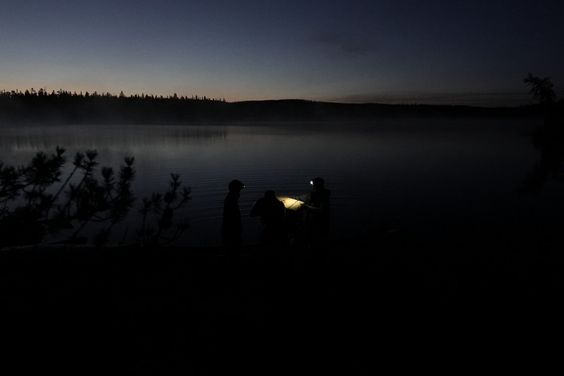 People using a lantern by a lake at dusk.