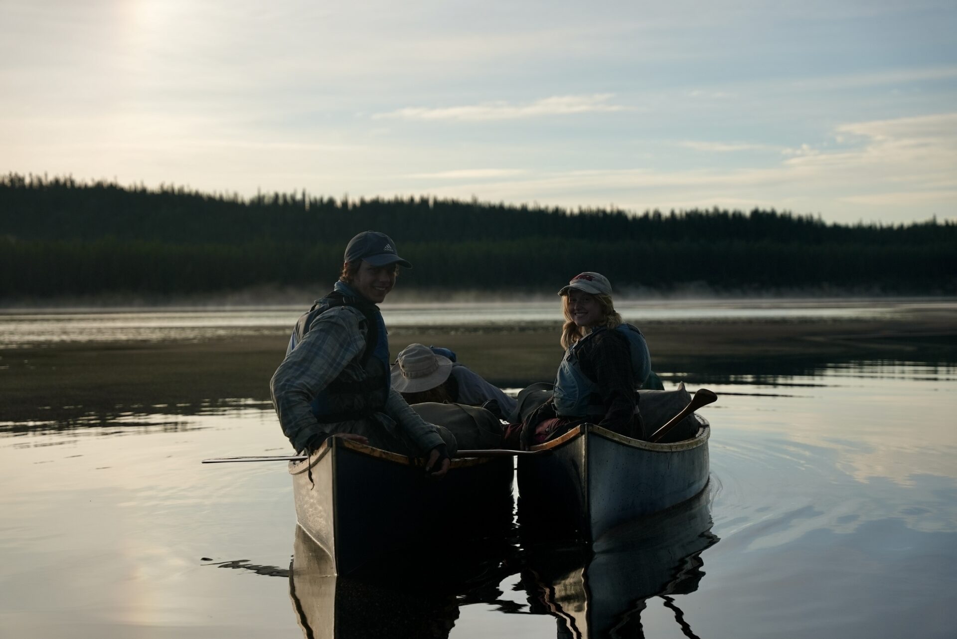 People canoeing on a calm lake at sunset.