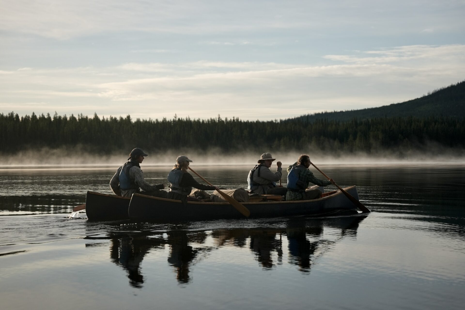 People canoeing on misty lake, forest background