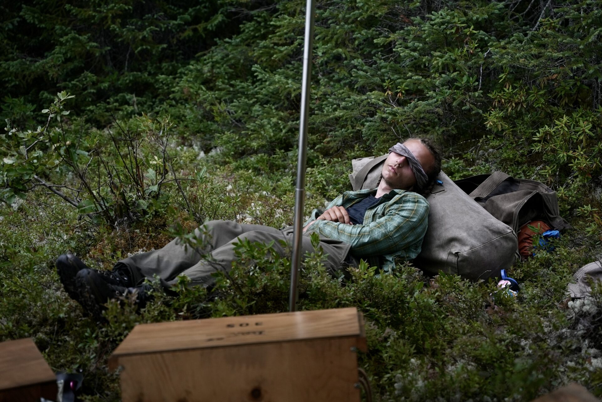 Person resting on woodland ground with eyes covered.