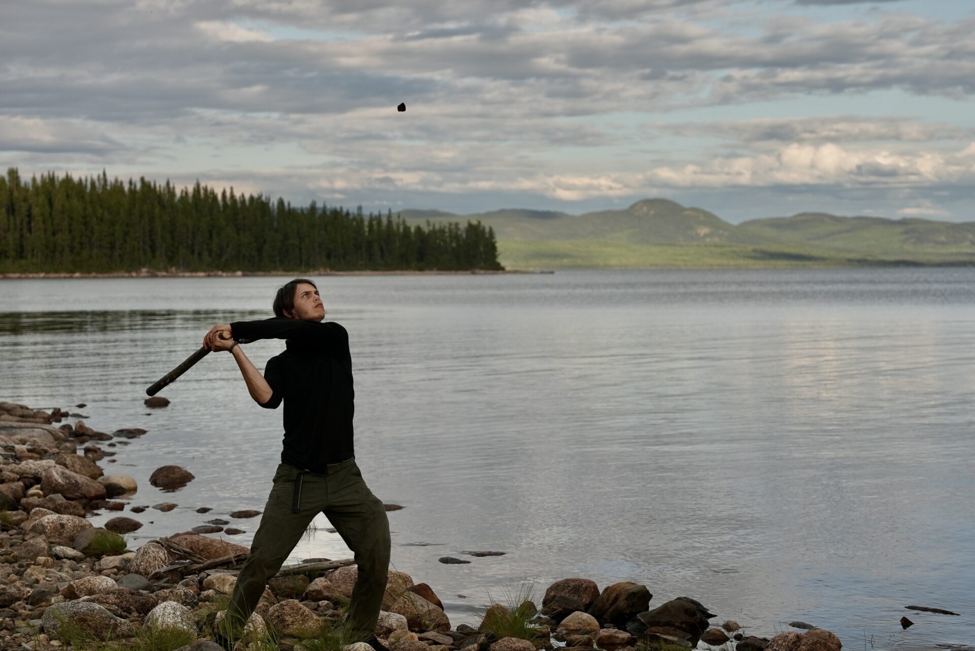 Person hitting rock with stick by a lake