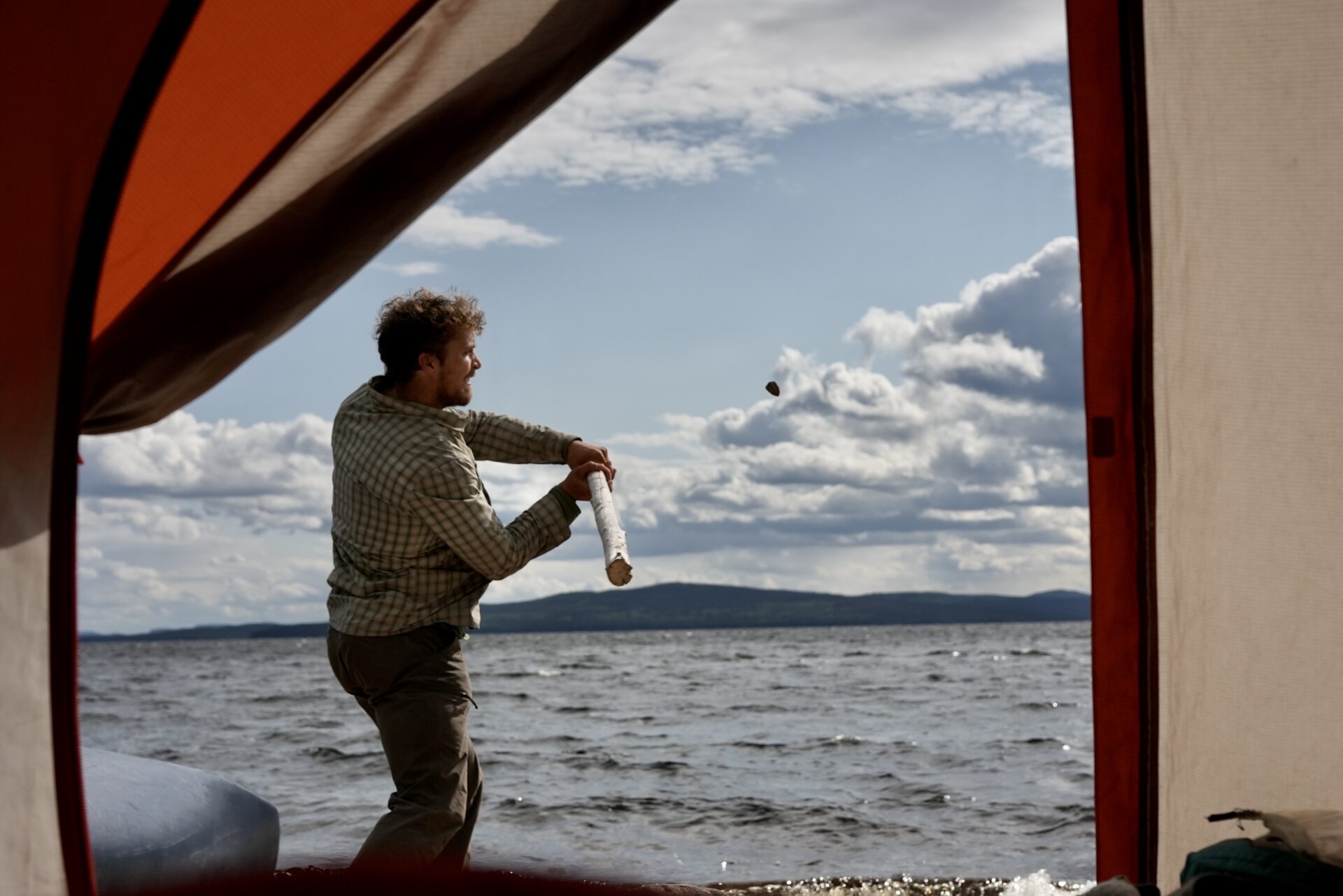 Man throws object outside tent near lake.