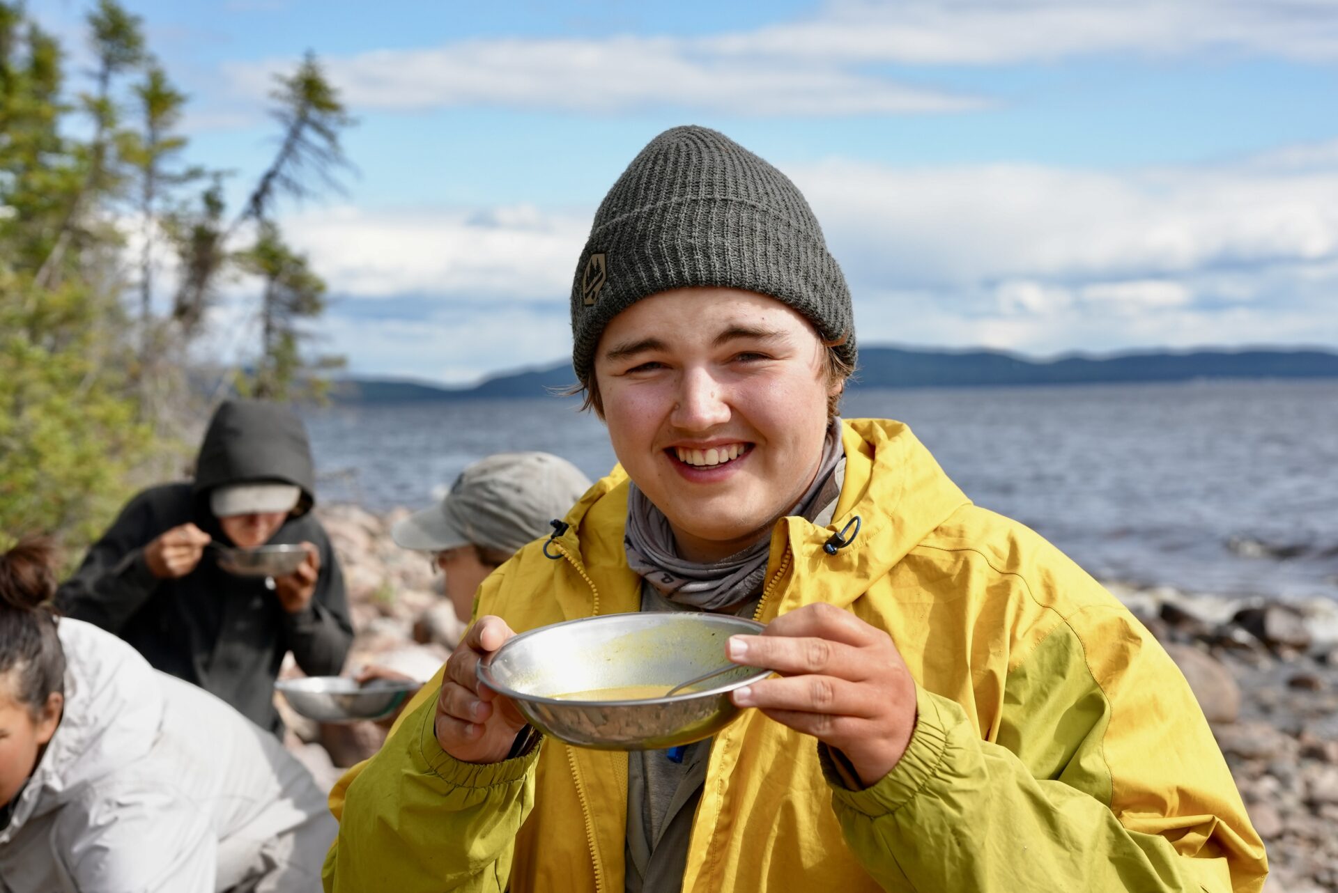 Person smiling, holding bowl near lake