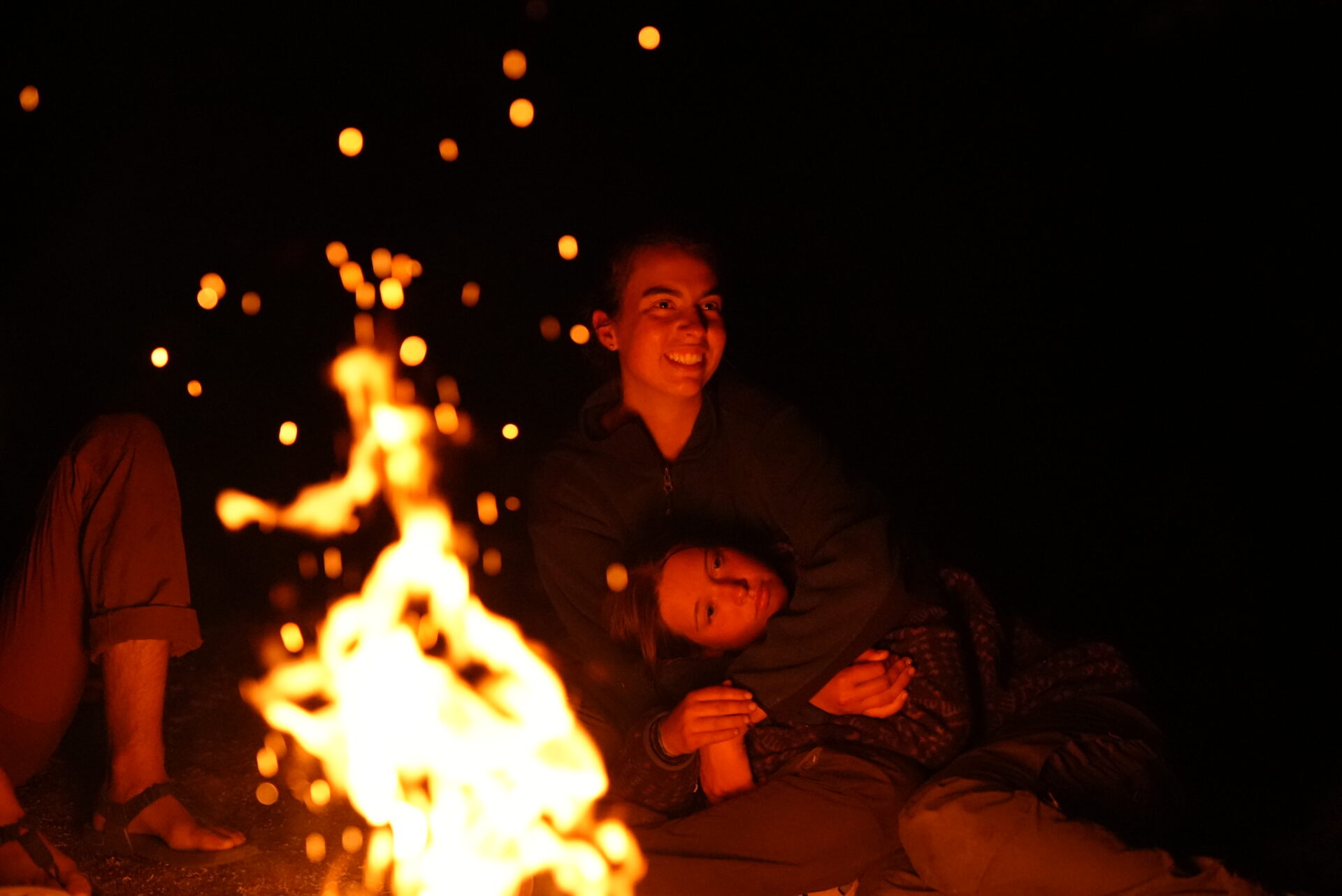 Two people sitting by a campfire.