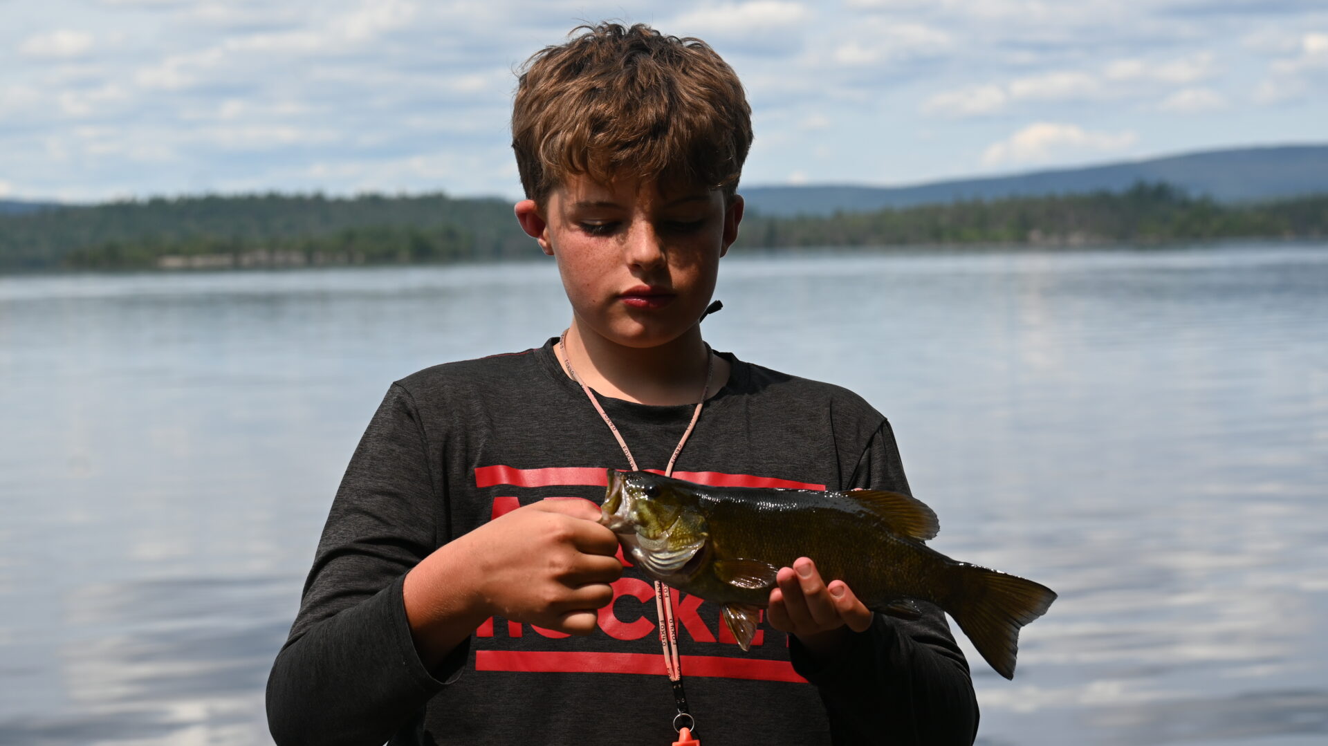 Boy holding a fish by the lake.