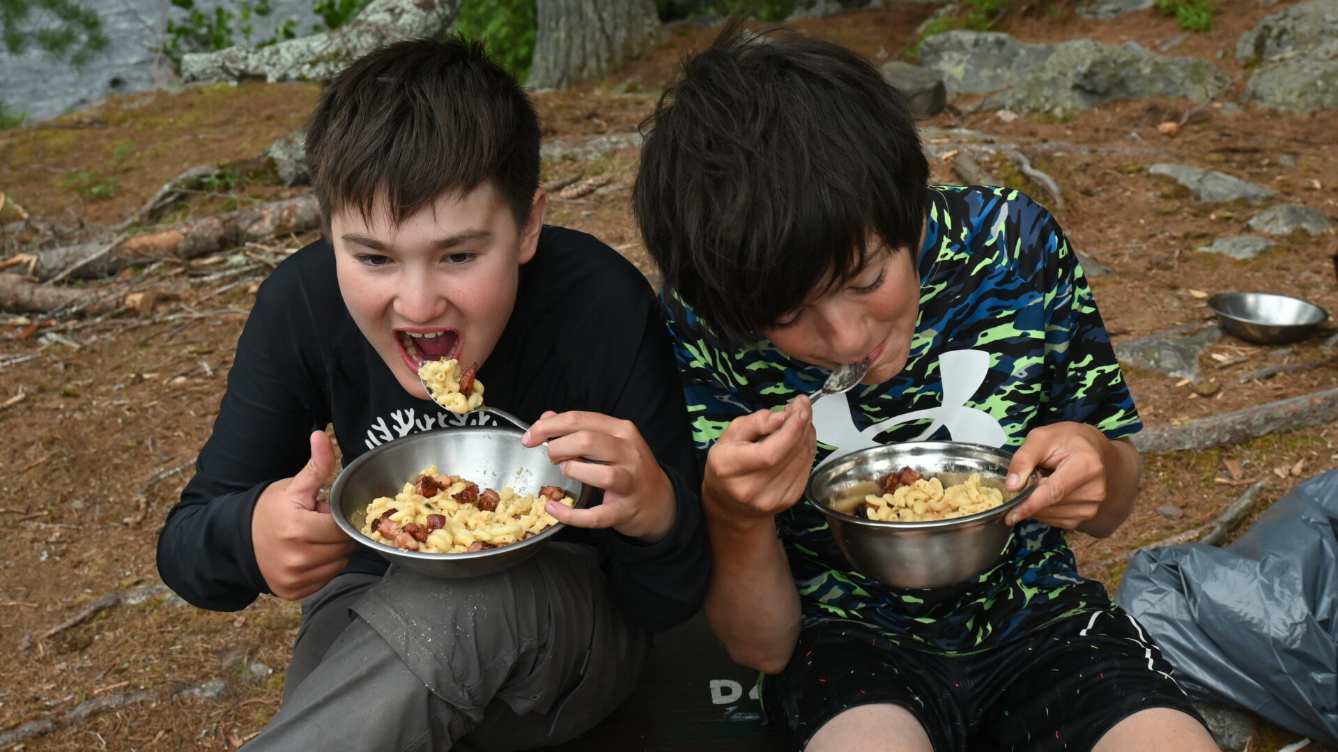 Two boys eating pasta outdoors.