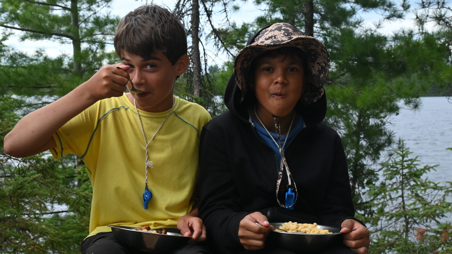 Two boys eating outdoors near a lake.