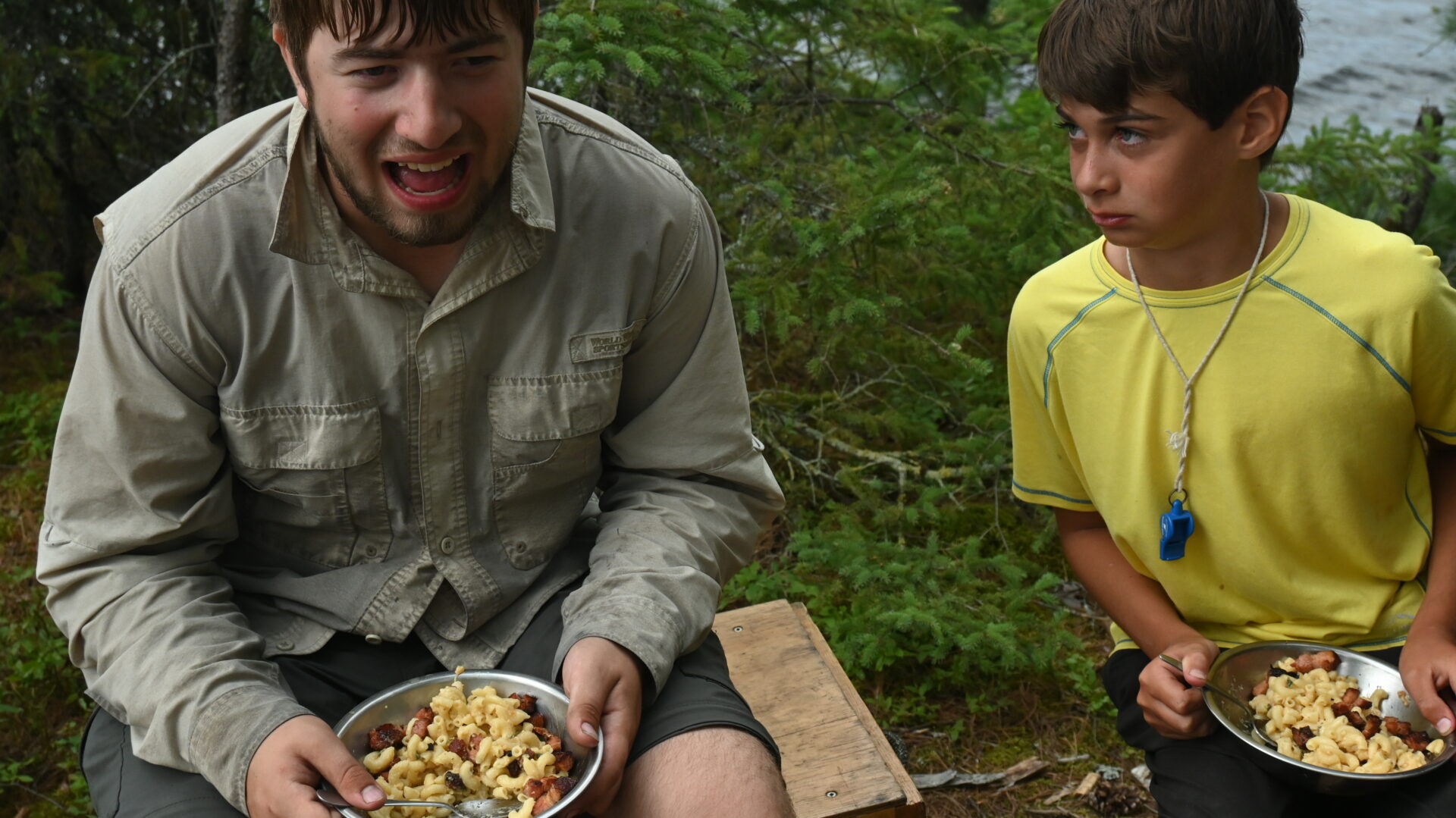 Two campers eating macaroni outside.