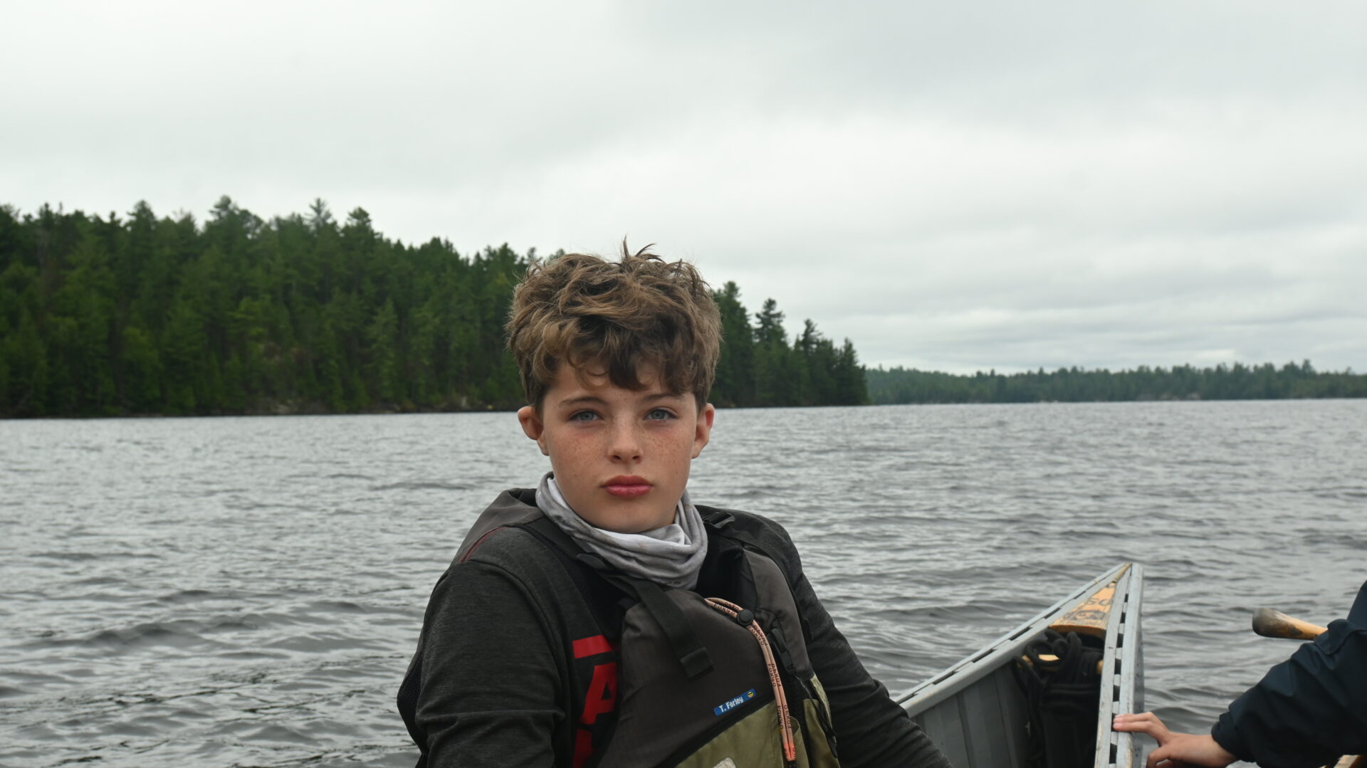 Boy canoeing on lake with forest backdrop.