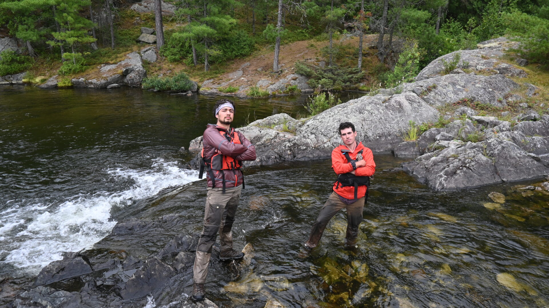 Two hikers pose by a river in the forest.