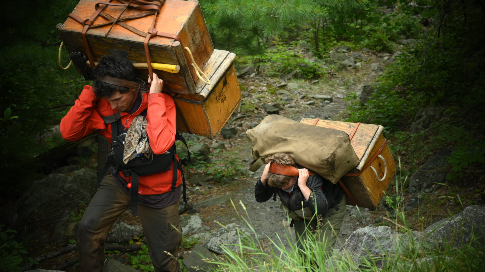 People carrying heavy wooden boxes through forest.