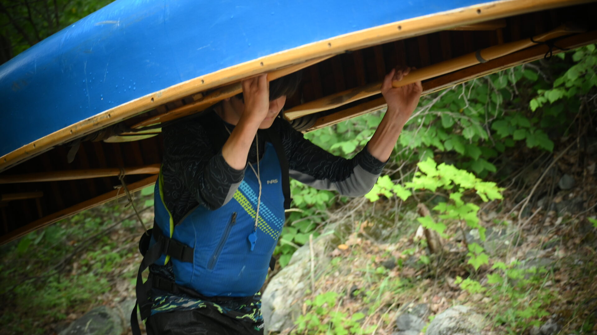 Person carrying canoe on shoulders in forest