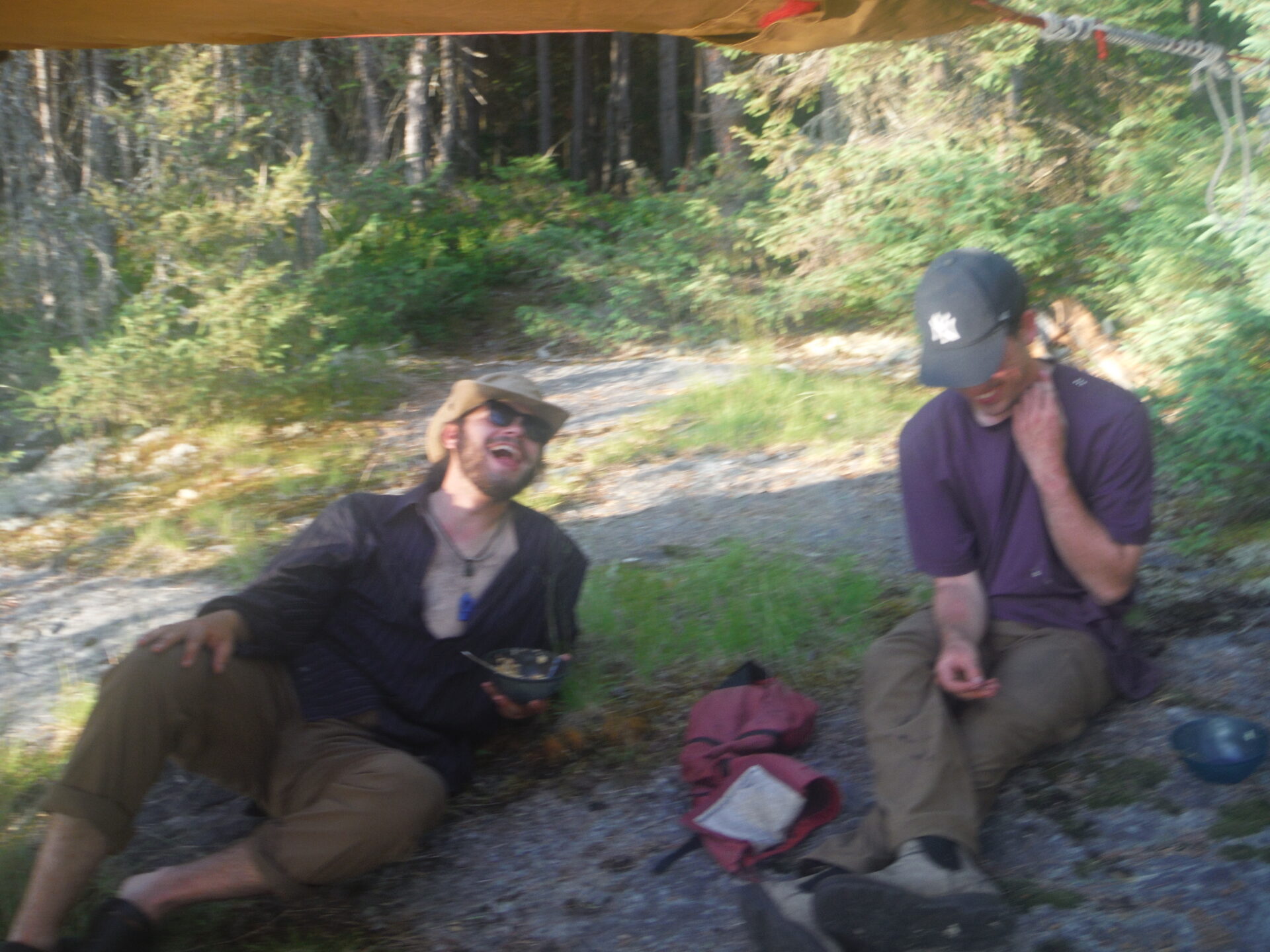 Two men laughing while sitting outdoors in nature.