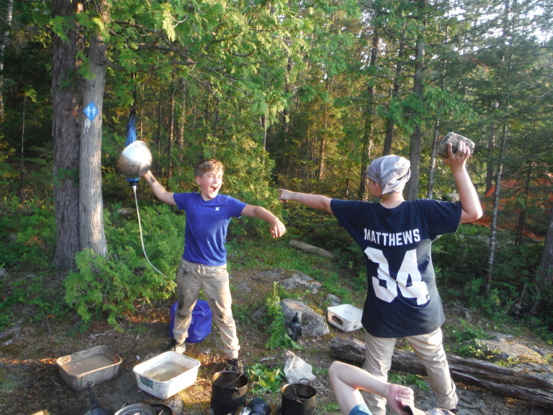 Two boys playing with camping gear in the forest.