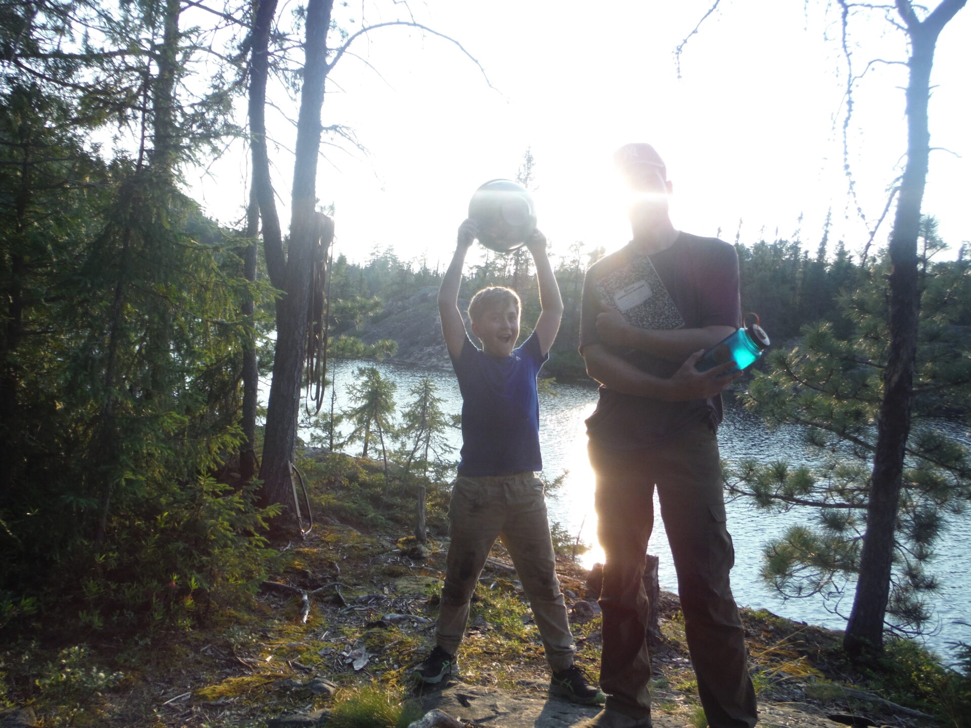 Two people hiking near a lake with trees.