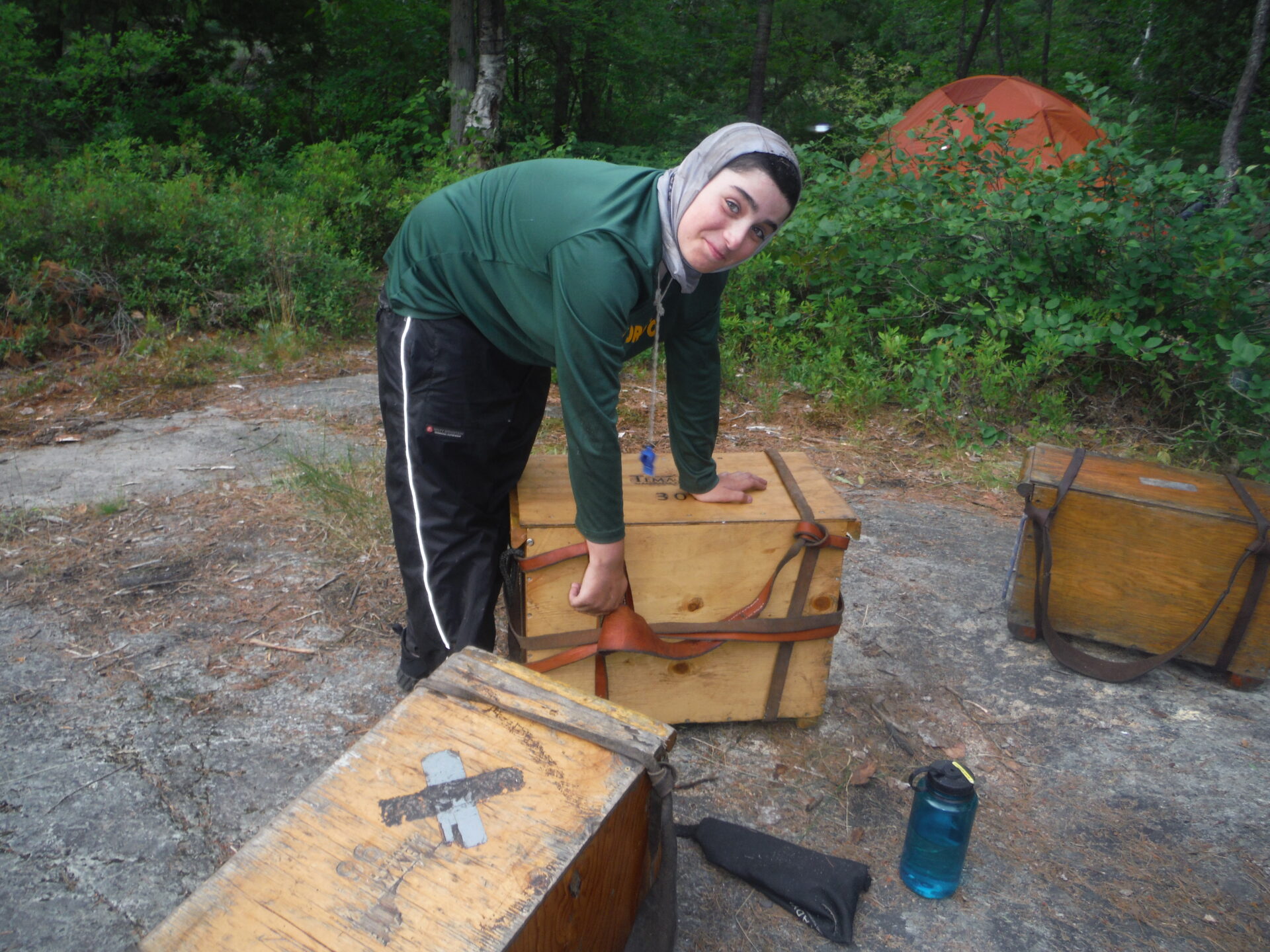 Person camping with wooden crates and tent in forest.