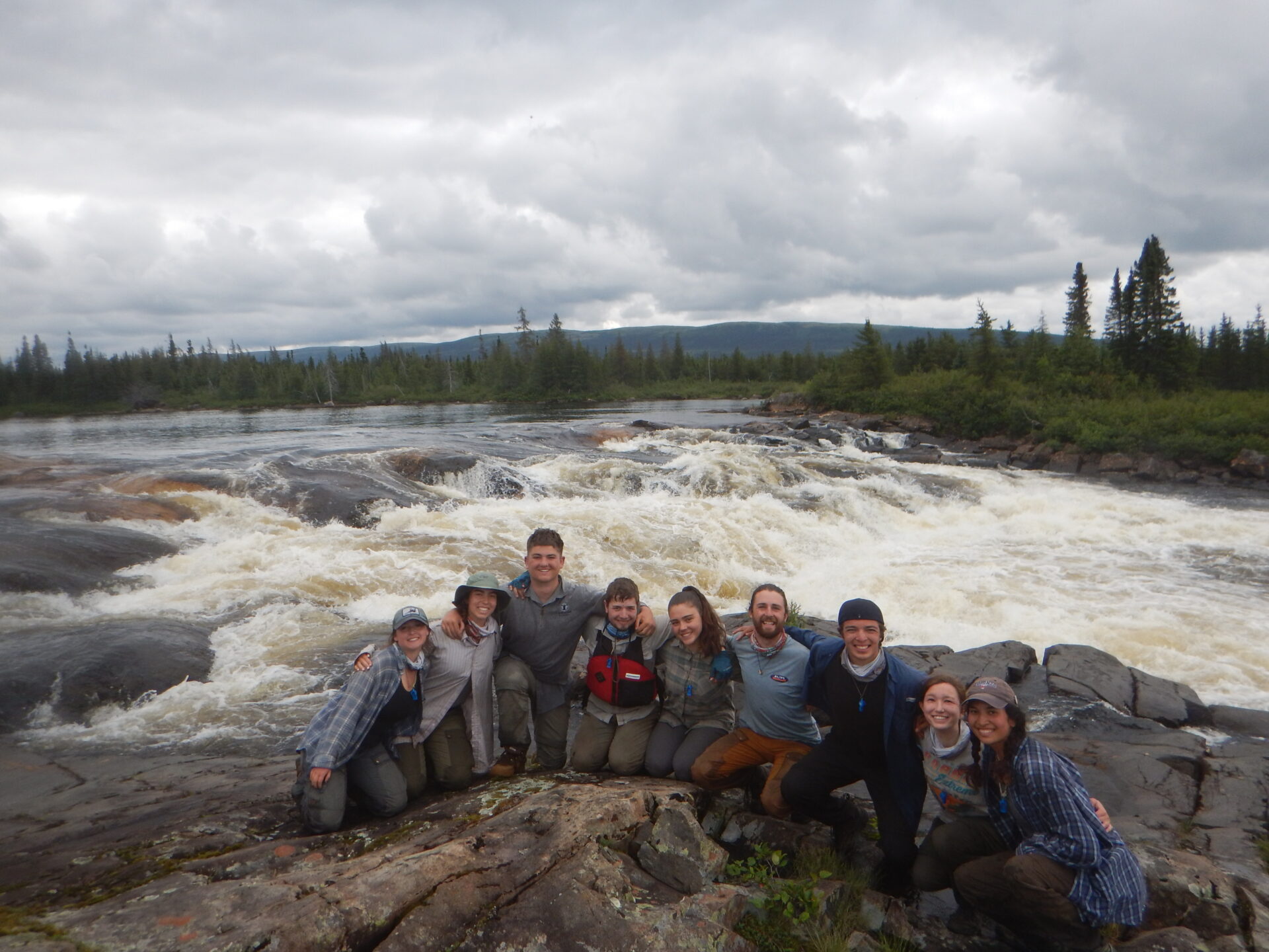 Group posing by a river with rapids.