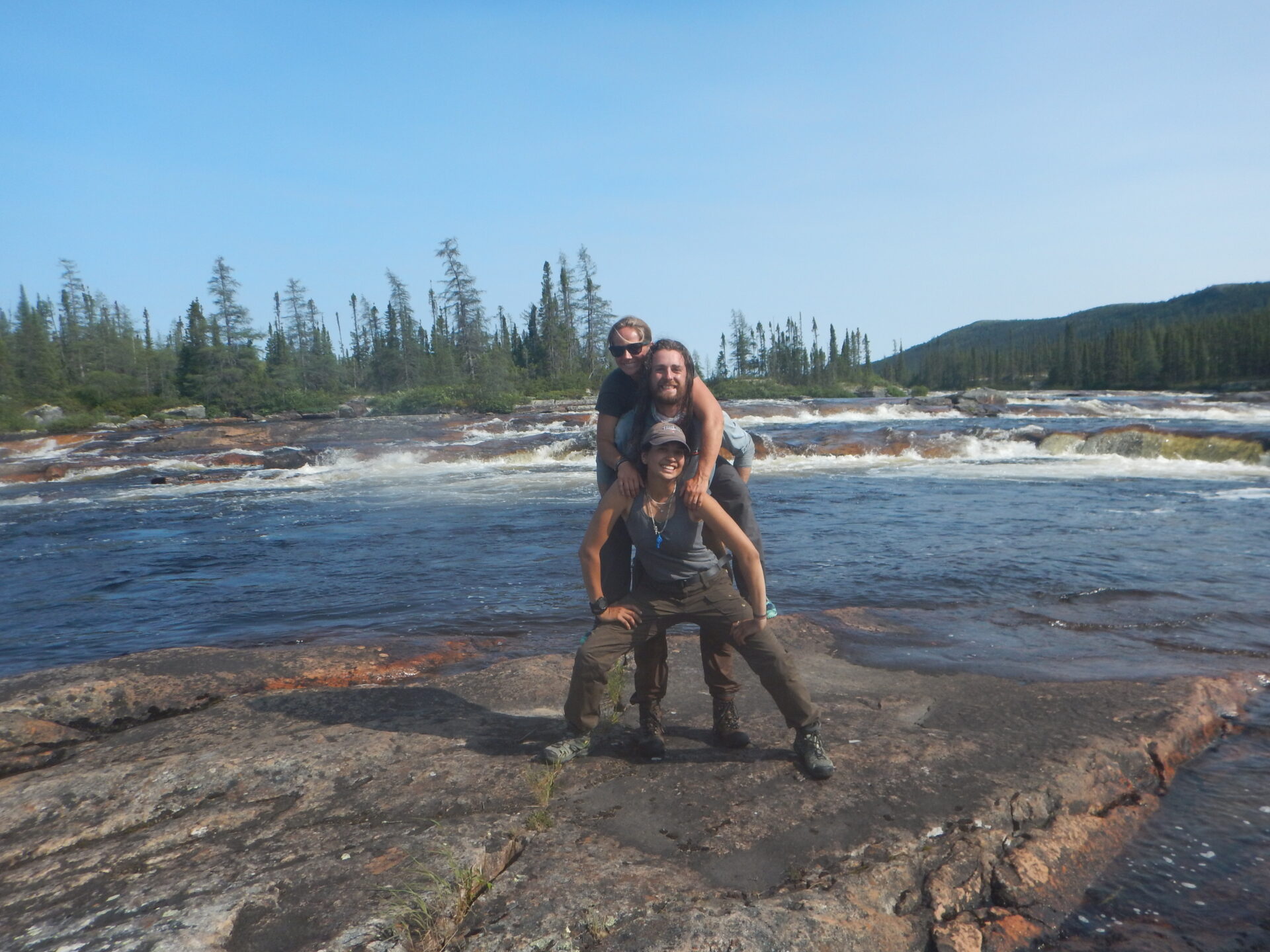 Three hikers pose by a scenic river