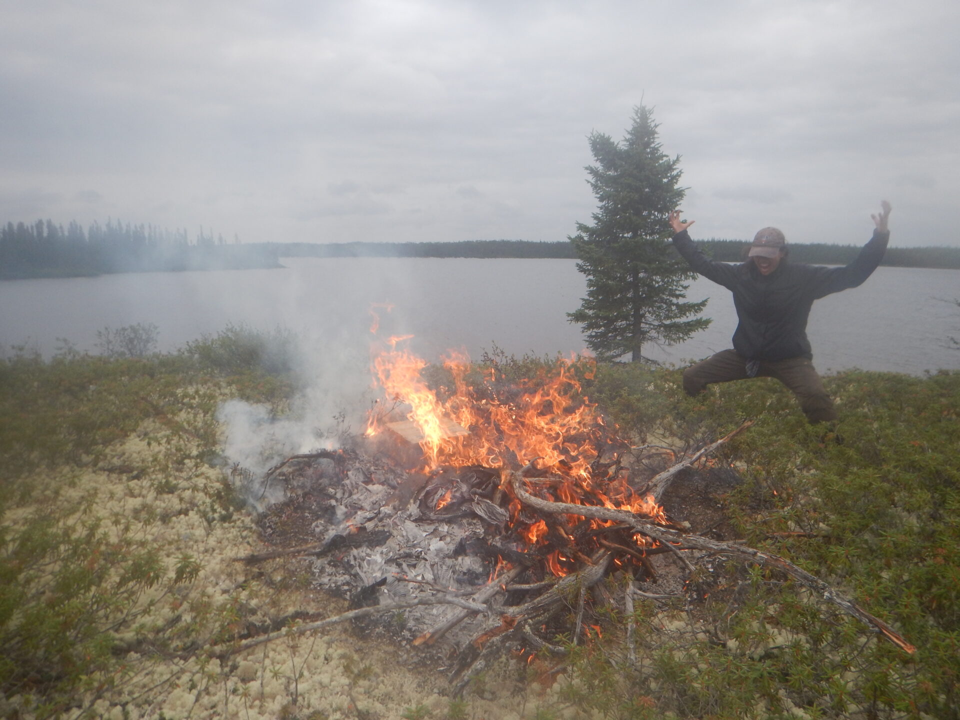 Person jumping near a bonfire by a lake