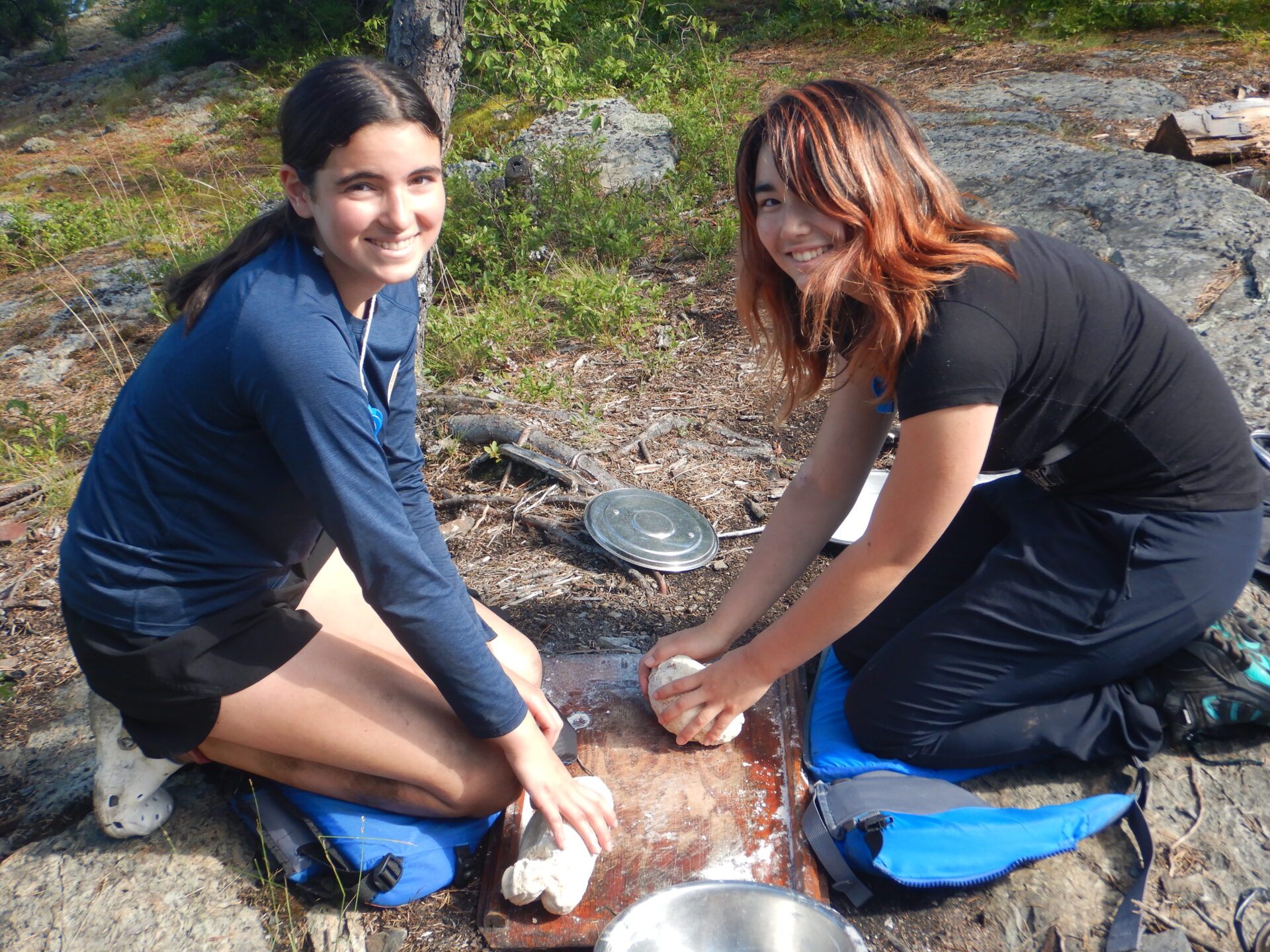 Two girls kneading dough outdoors on a sunny day.