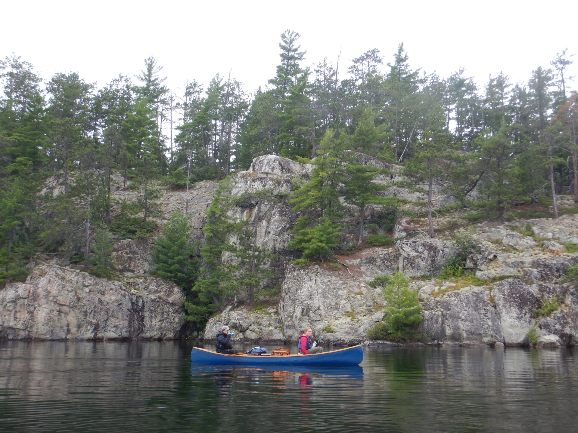 Two people canoeing on a lake by rocky shore