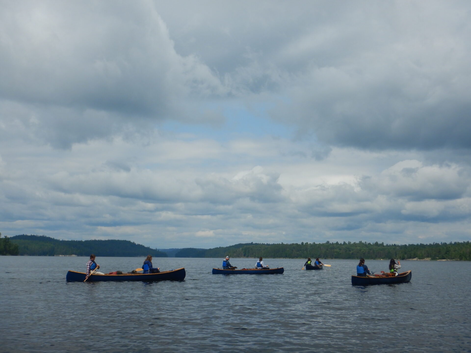 People canoeing on a lake under cloudy sky.