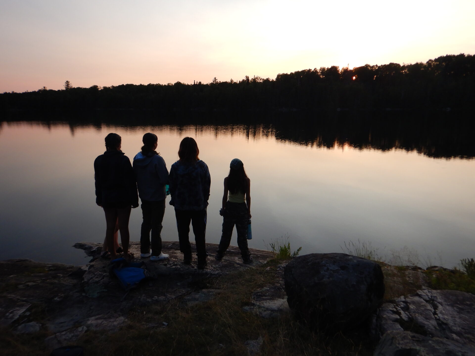 People standing by a tranquil lake at sunset.