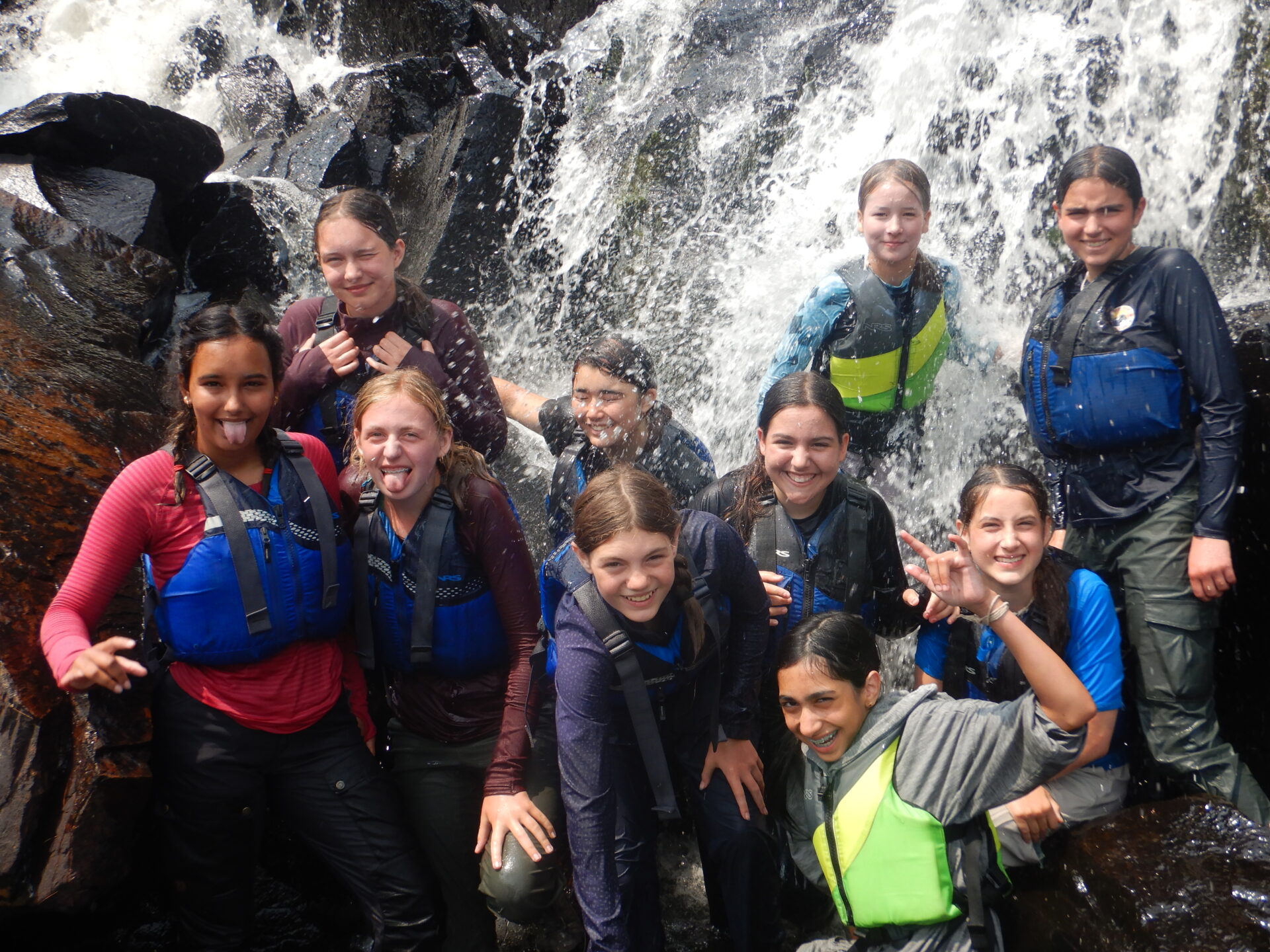 Group of kids smiling in front of waterfall.