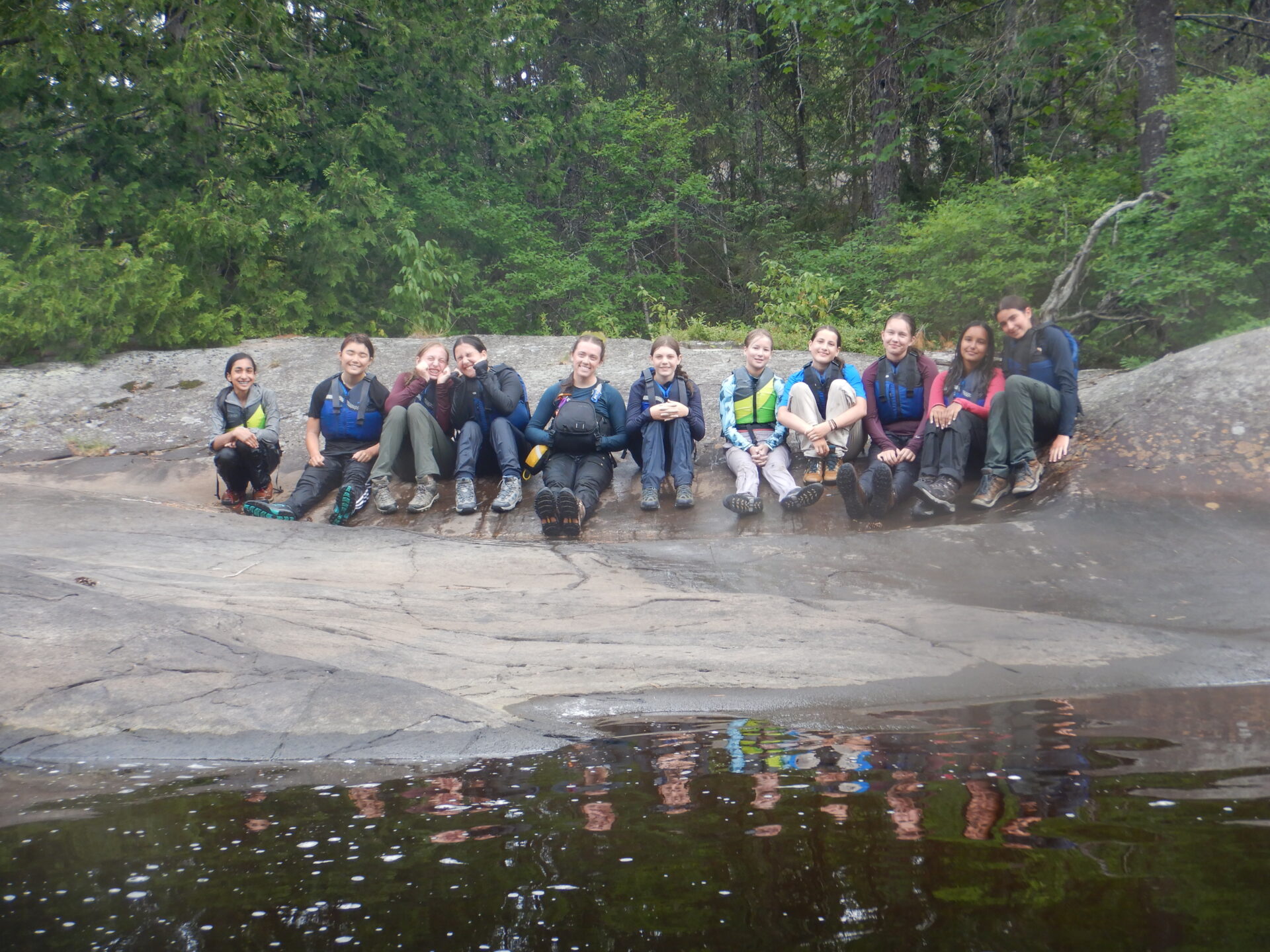 Group of friends sitting on rocks by water.